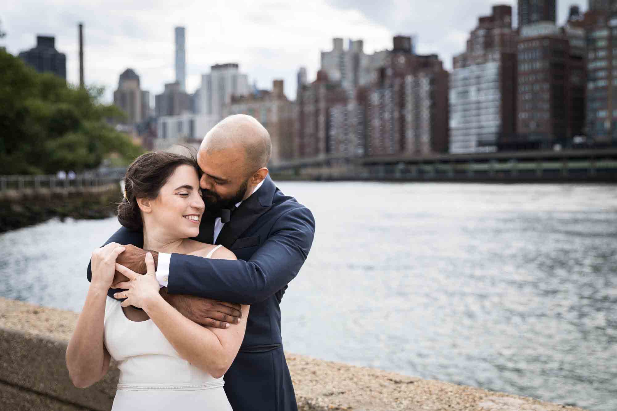 Bride and groom hugging in front of NYC skyline on Roosevelt Island