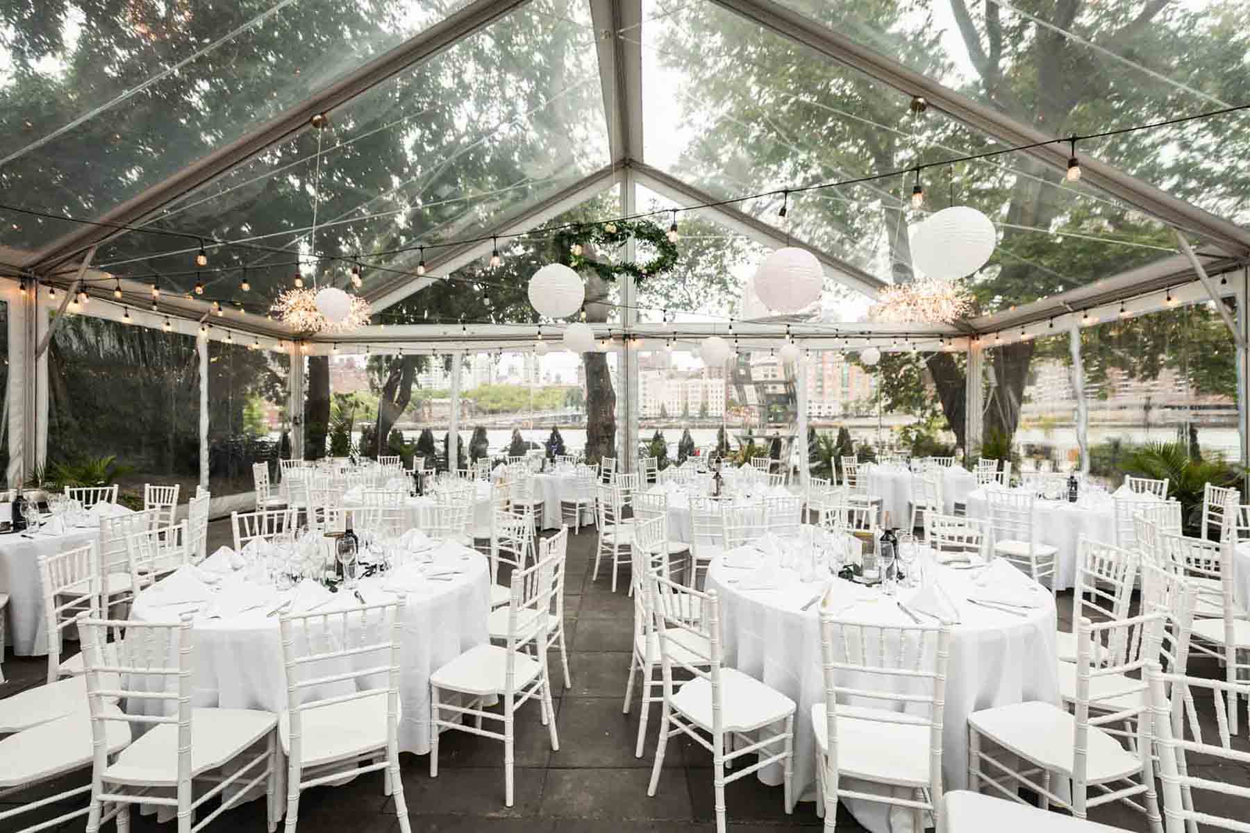 Tables set with glasses and white chairs under clear tent at a Sanctuary Roosevelt Island wedding