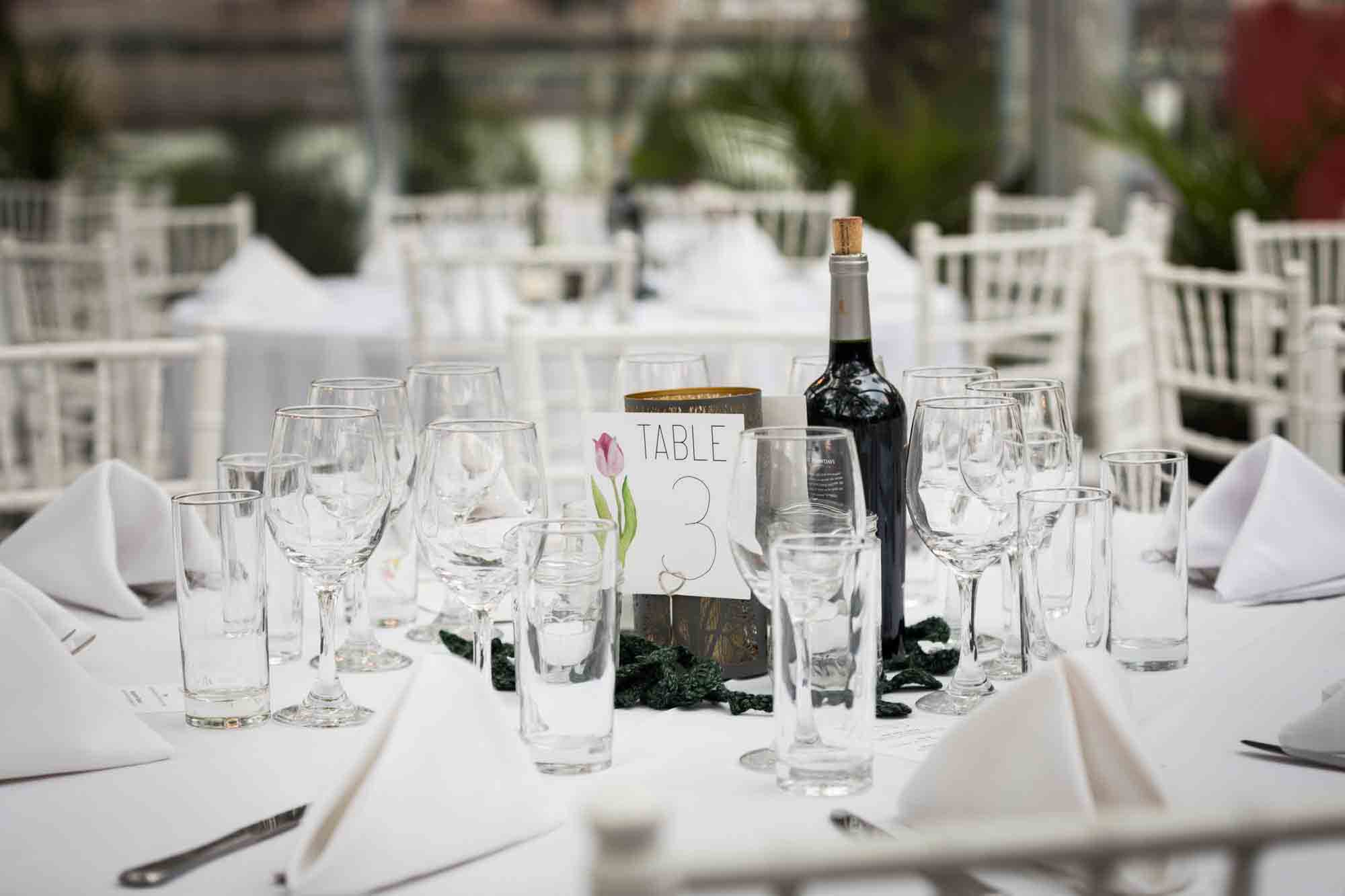 Table setting with glasses, table 3 sign, and wine bottle at a Sanctuary Roosevelt Island wedding