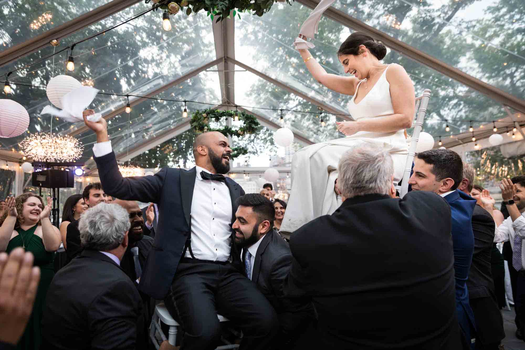 Bride and groom held in air twirling napkins during the hora at a Sanctuary Roosevelt Island wedding