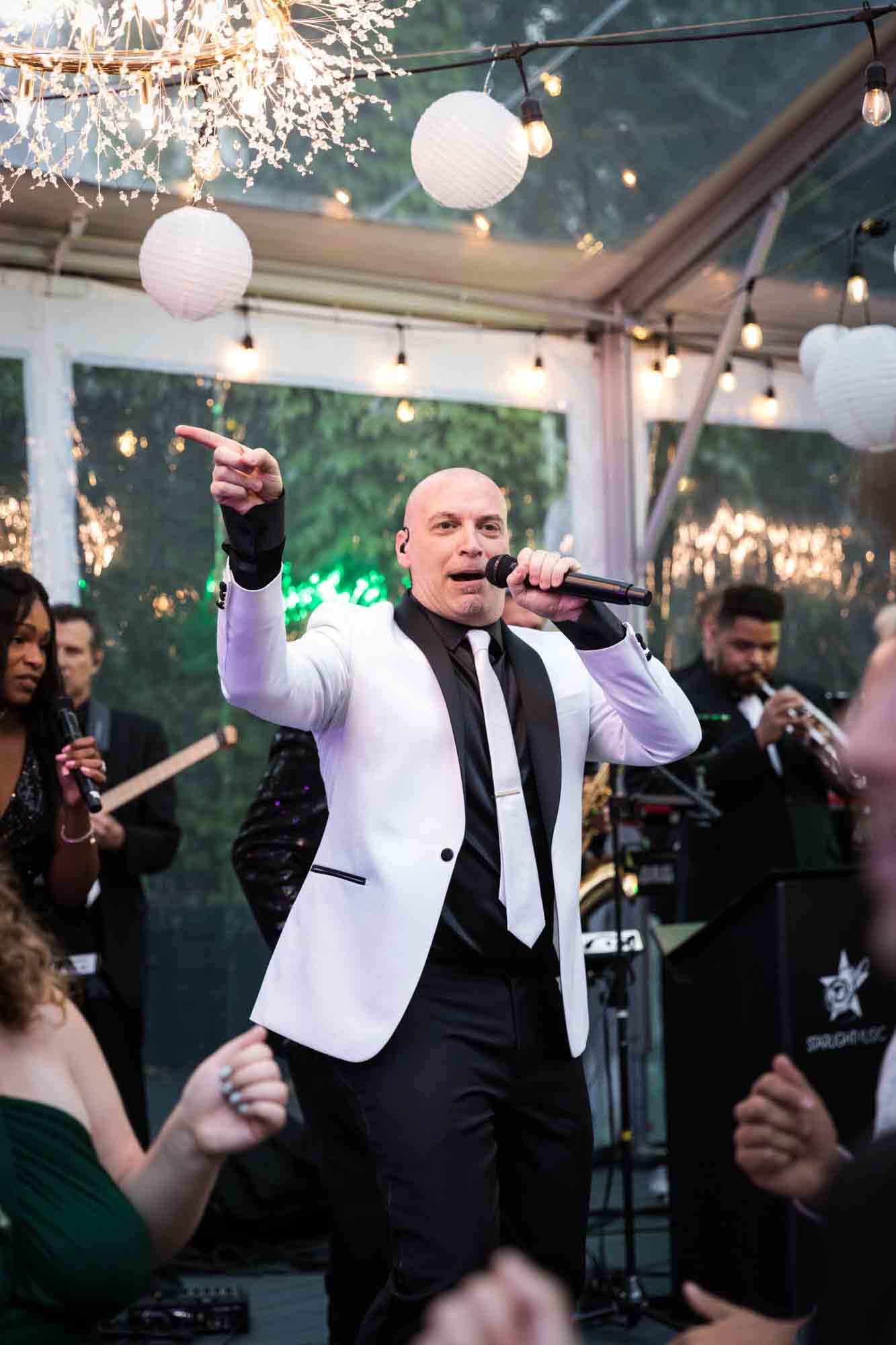 Man in white tuxedo singing into microphone at a Sanctuary Roosevelt Island wedding