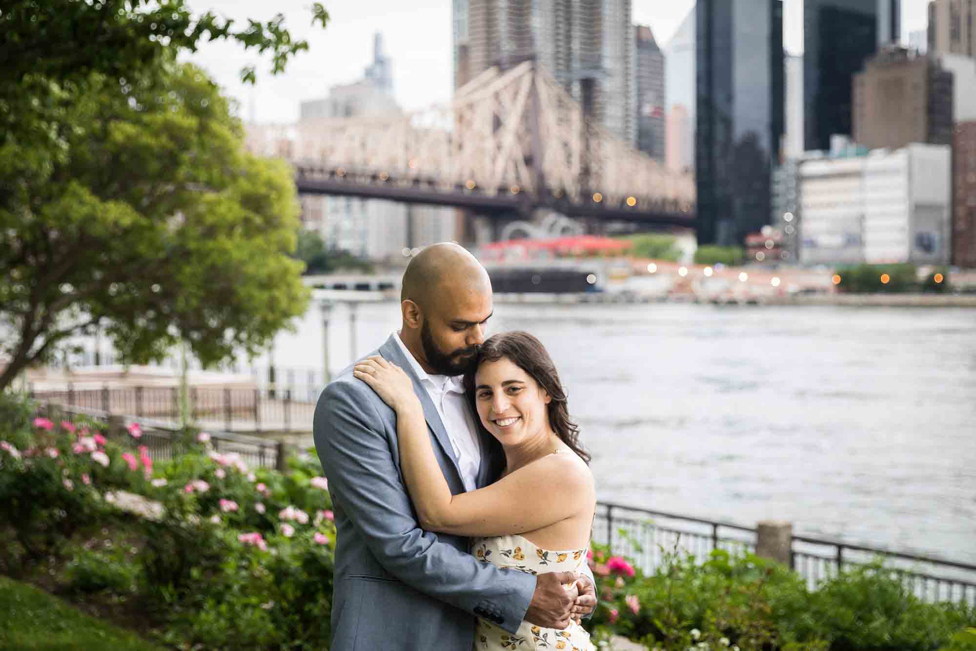 Man and woman hugging in park with Queensborough Bridge and East River in background