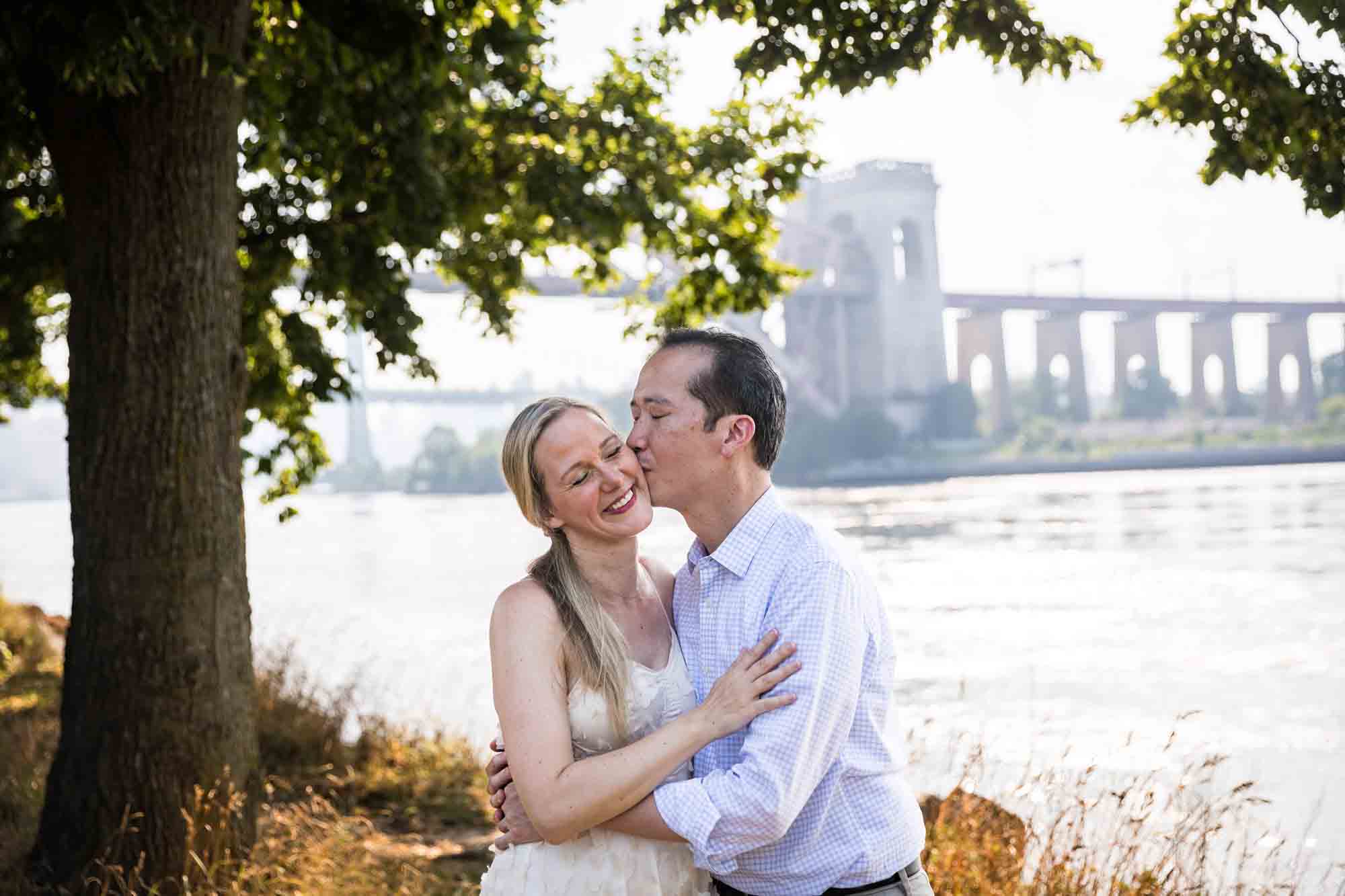 Astoria Park engagement photos of a man kissing woman on the cheek along waterfront