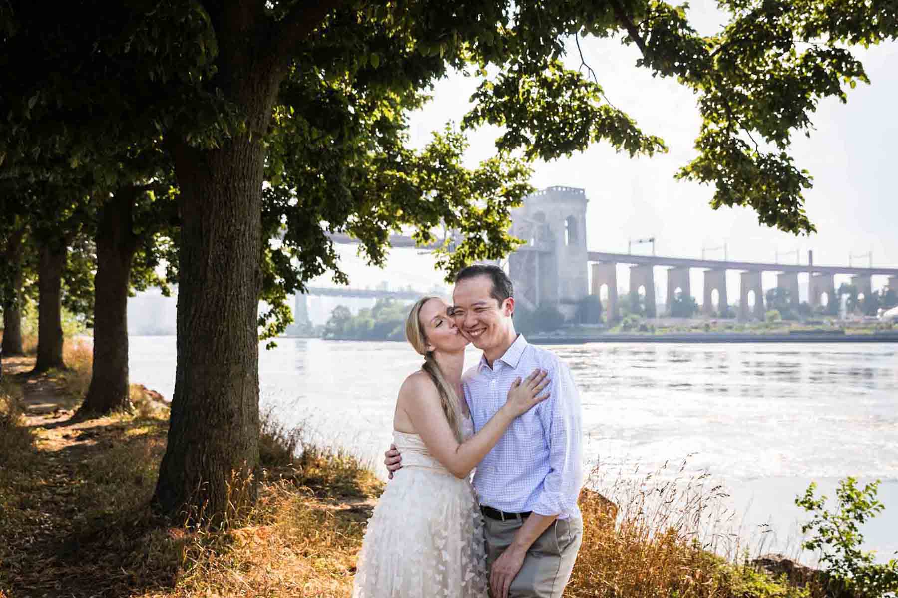 Astoria Park engagement photos of a woman kissing man on the cheek along waterfront