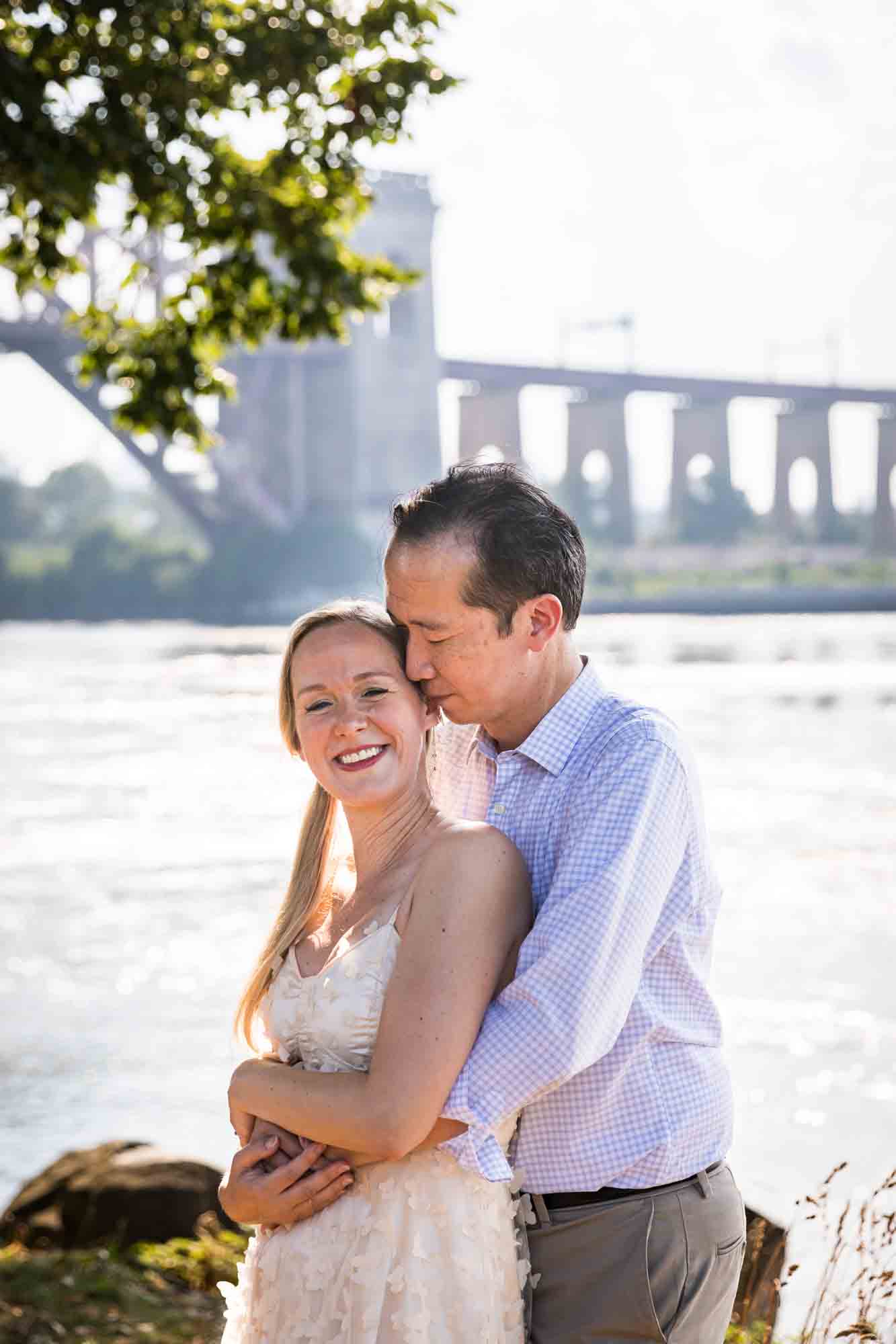 Astoria Park engagement photos of a man kissing woman on cheek along waterfront