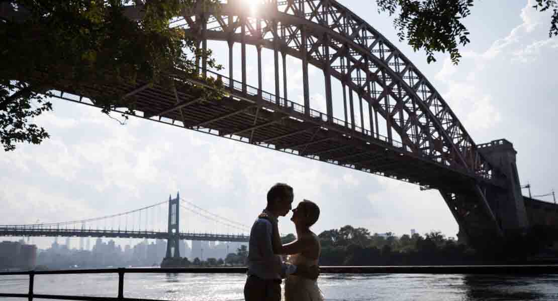 Astoria Park engagement photos of a couple under Hell Gate Bridge in backlit lighting