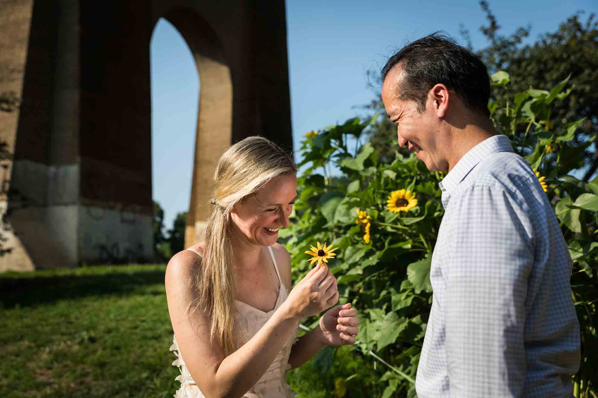 Astoria Park engagement photos of a man giving a sunflower to a woman under Hell Gate Bridge