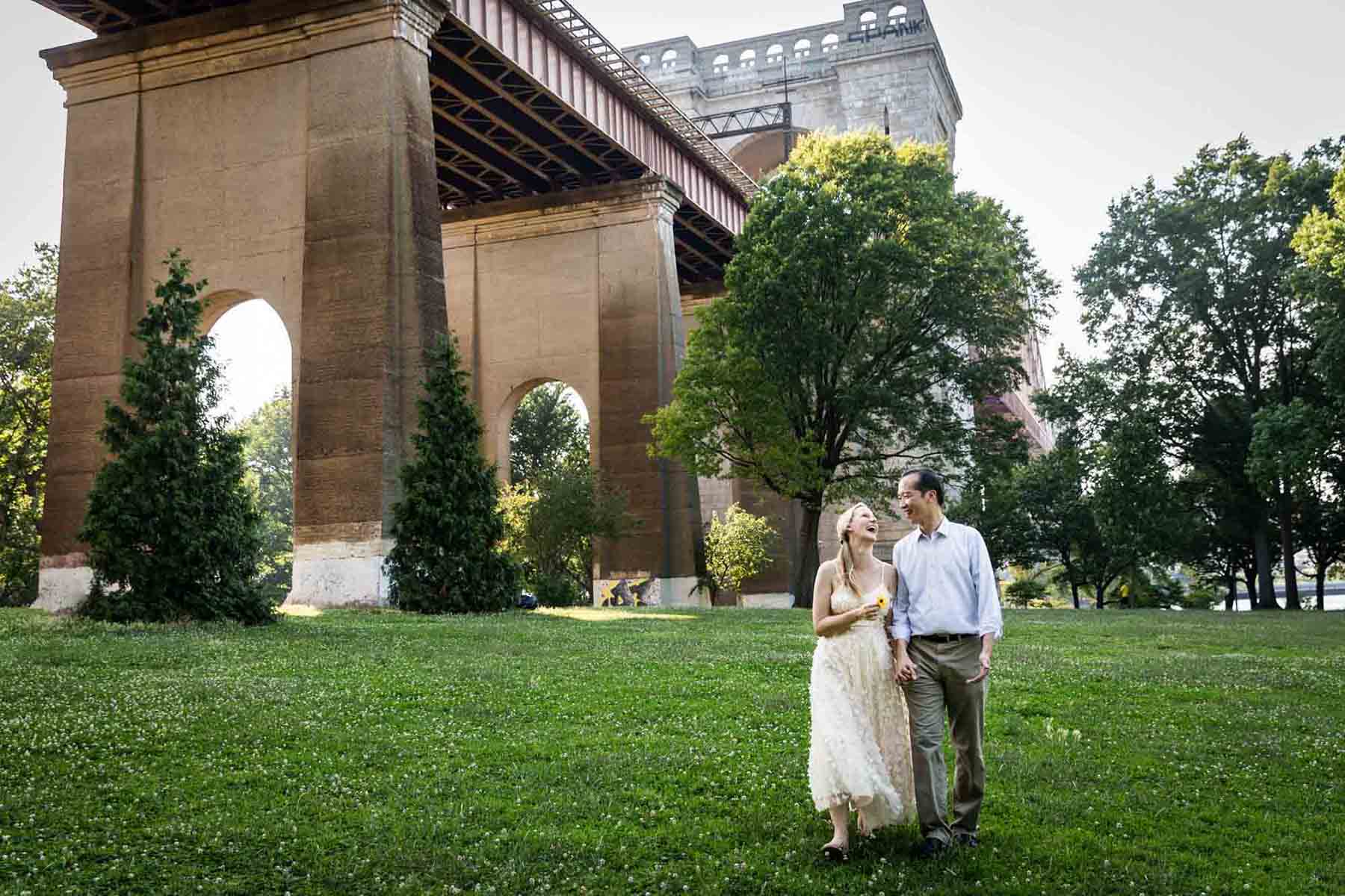 Astoria Park engagement photos of a couple walking in front of Hell Gate Bridge