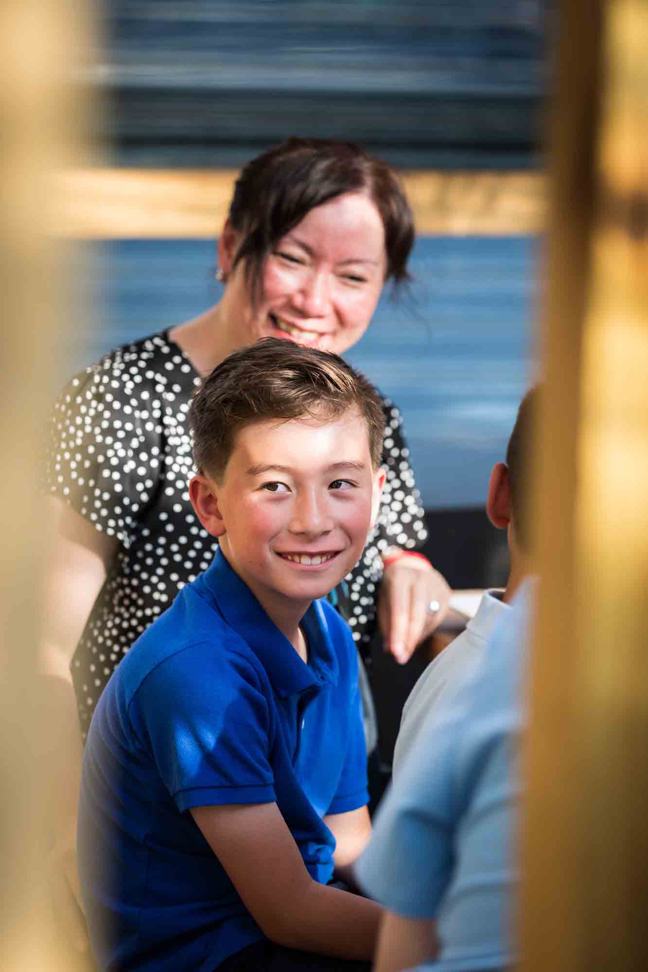 Little boy in blue smiling while seated at an outdoor restaurant during rehearsal dinner