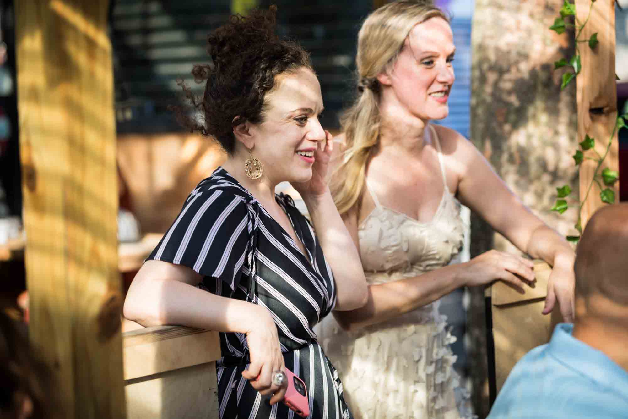 Two women laughing and talking during rehearsal dinner at an outdoor restaurant