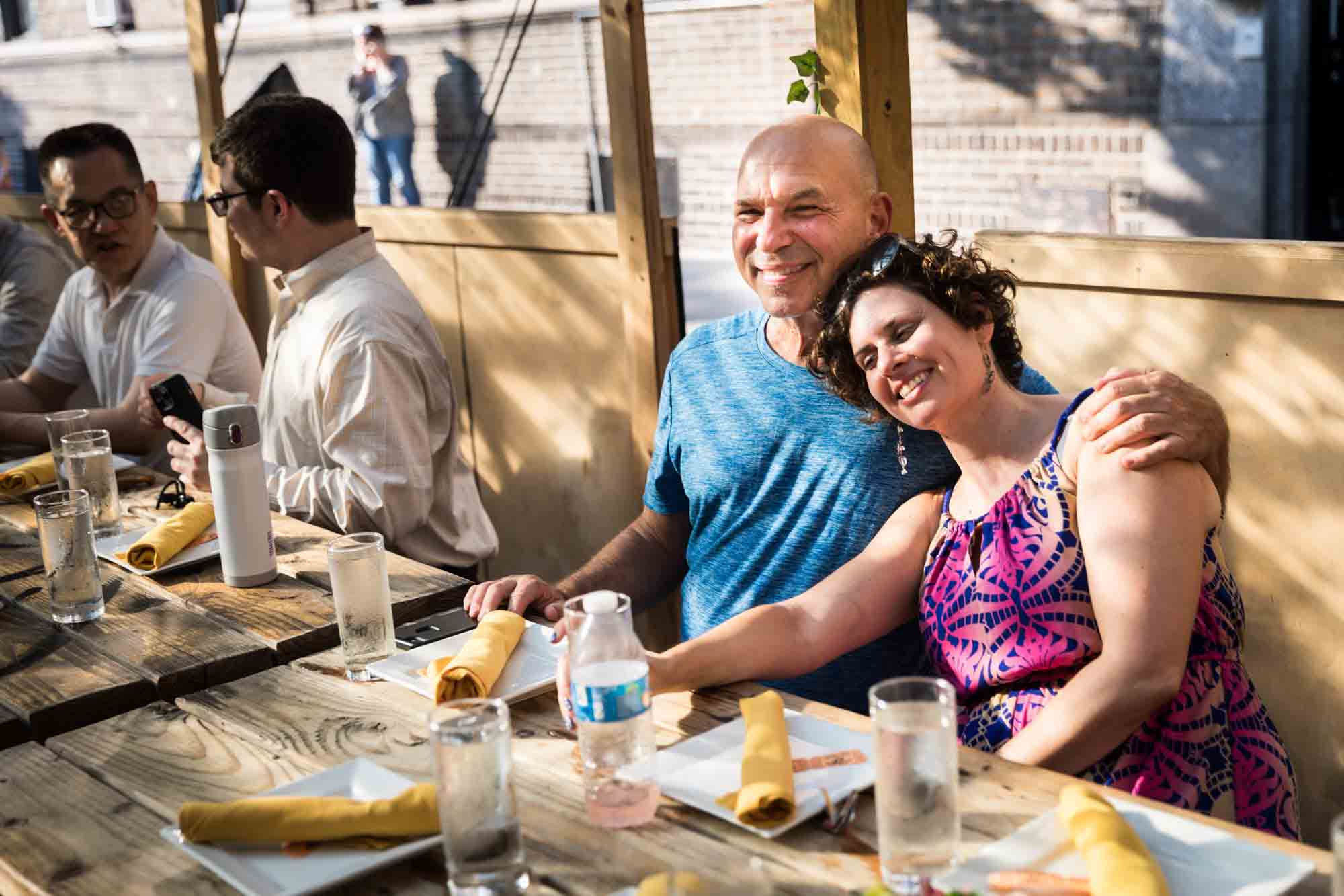 Woman leaning on man at dinner table during rehearsal dinner at an outdoor restaurant