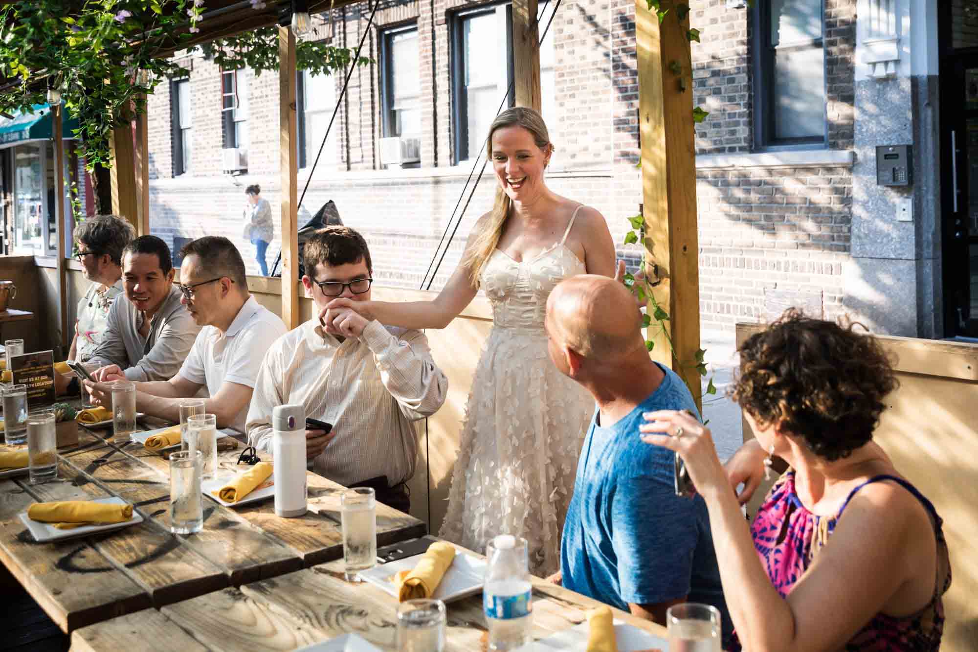 Bride talking to seated guests during rehearsal dinner at an outdoor restaurant