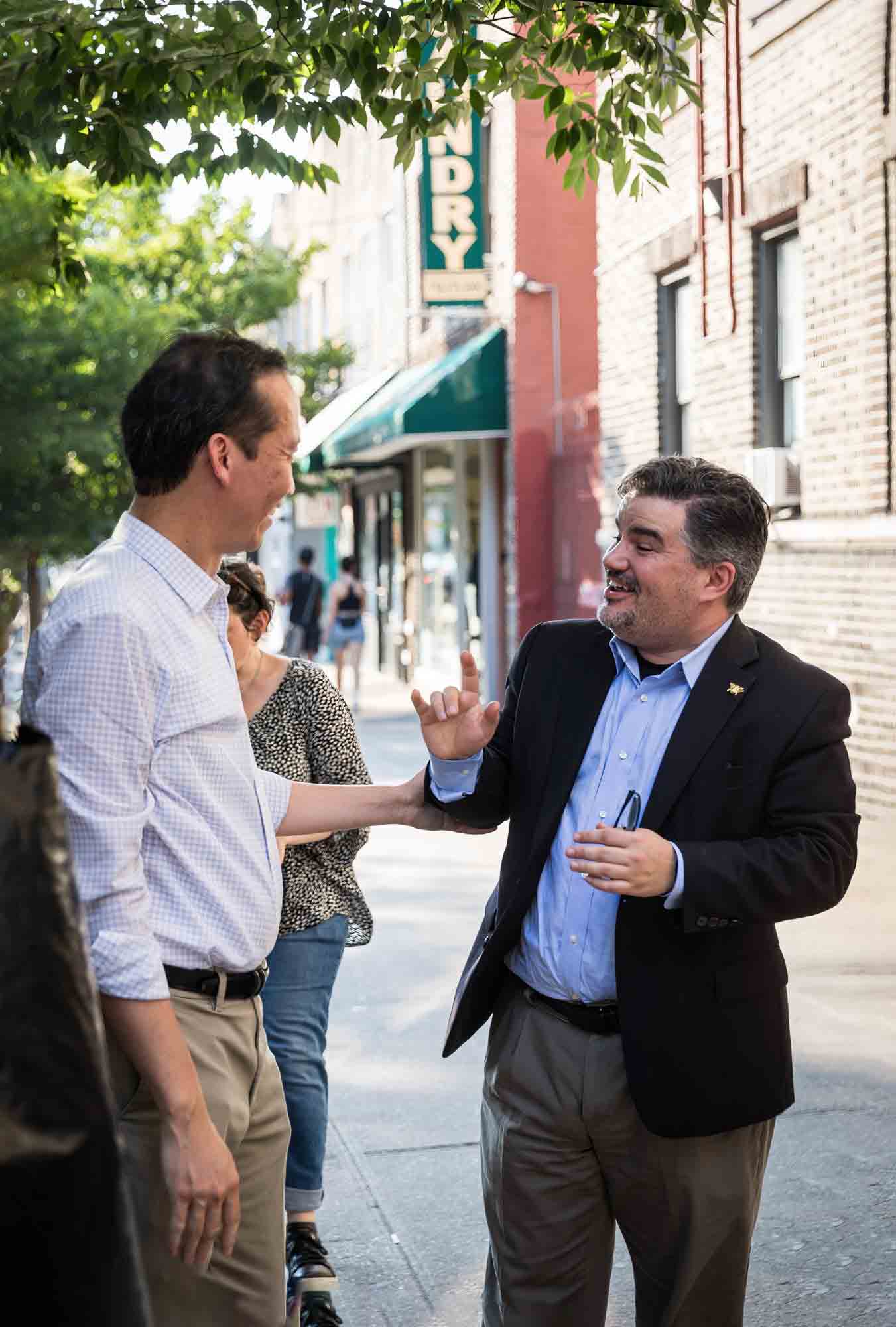 Groom speaking to man wearing a blazer during rehearsal dinner at an outdoor restaurant