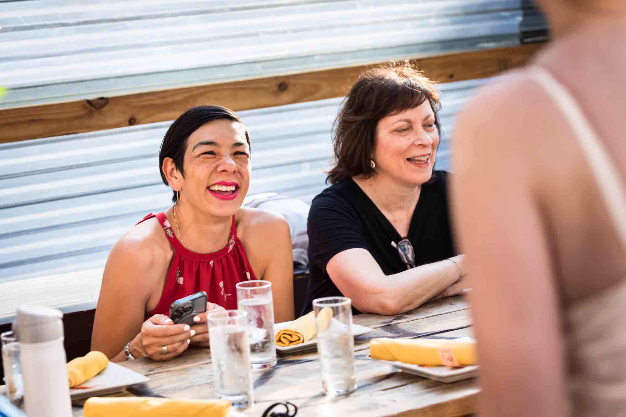Two women smiling while seated during rehearsal dinner at an outdoor restaurant