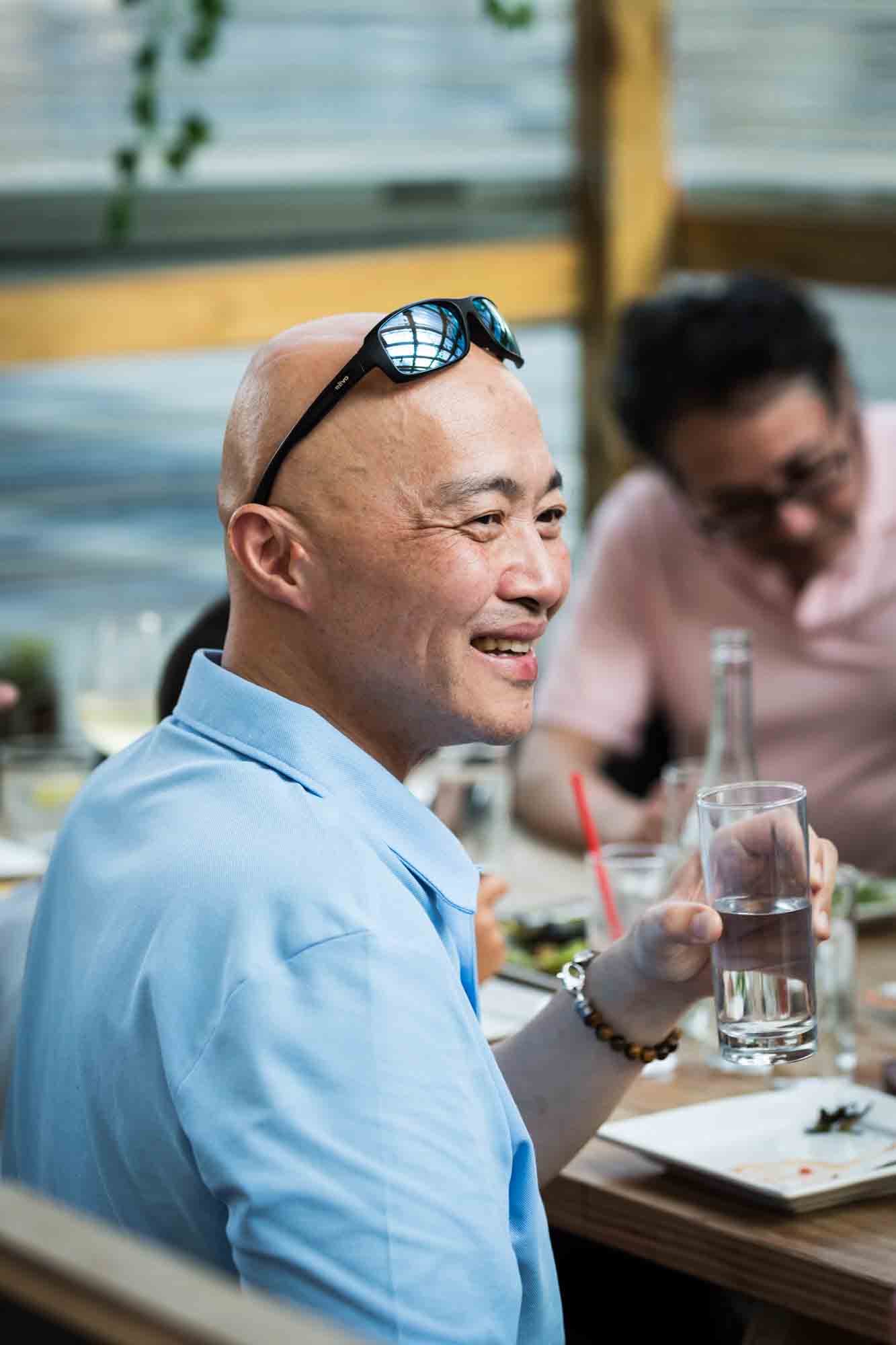 Bald Asian man with sunglasses on his head during rehearsal dinner at an outdoor restaurant