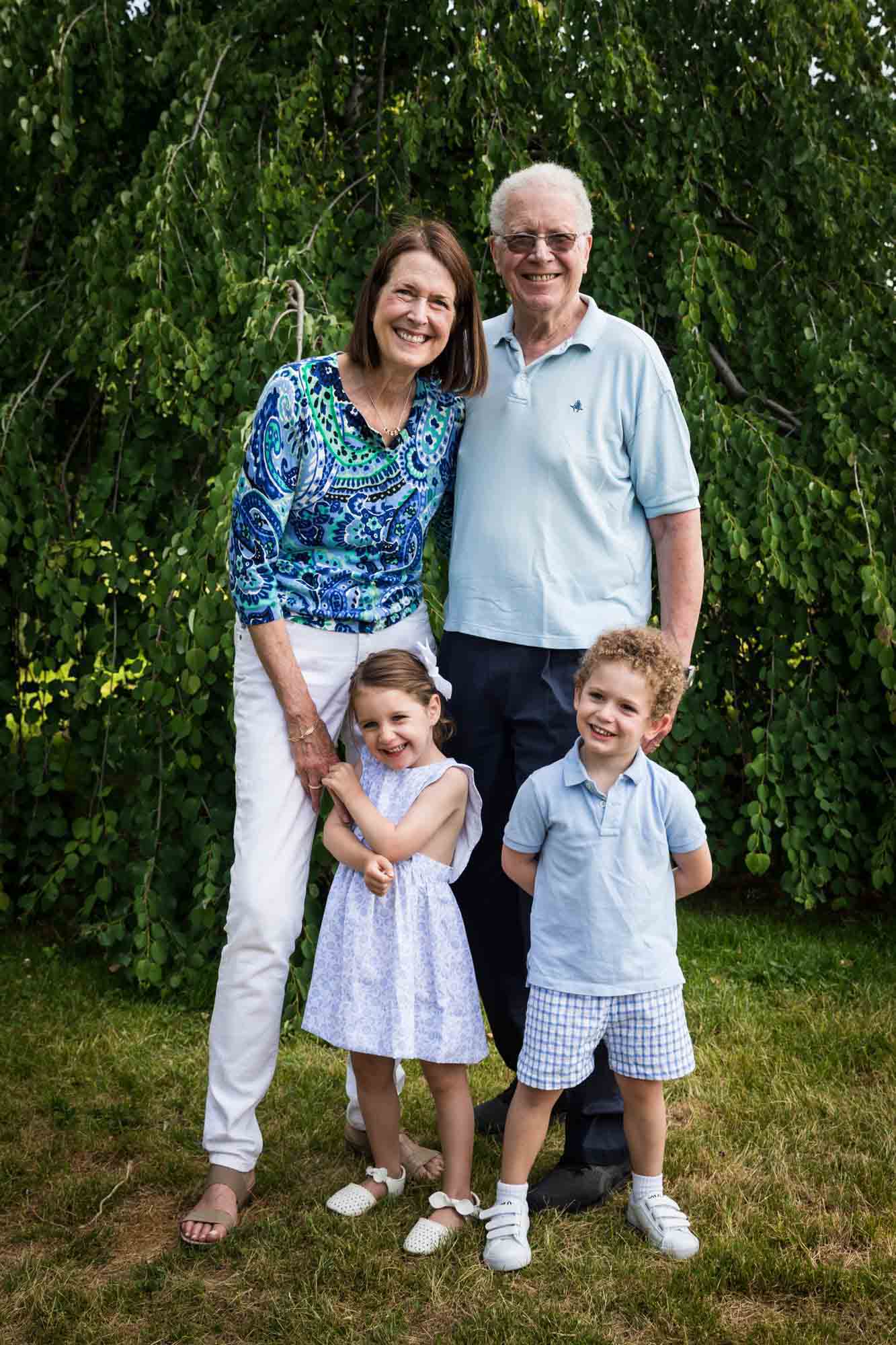 Grandparents standing with a little boy and girl in front of a tree during a Narrows Botanical Gardens family portrait session