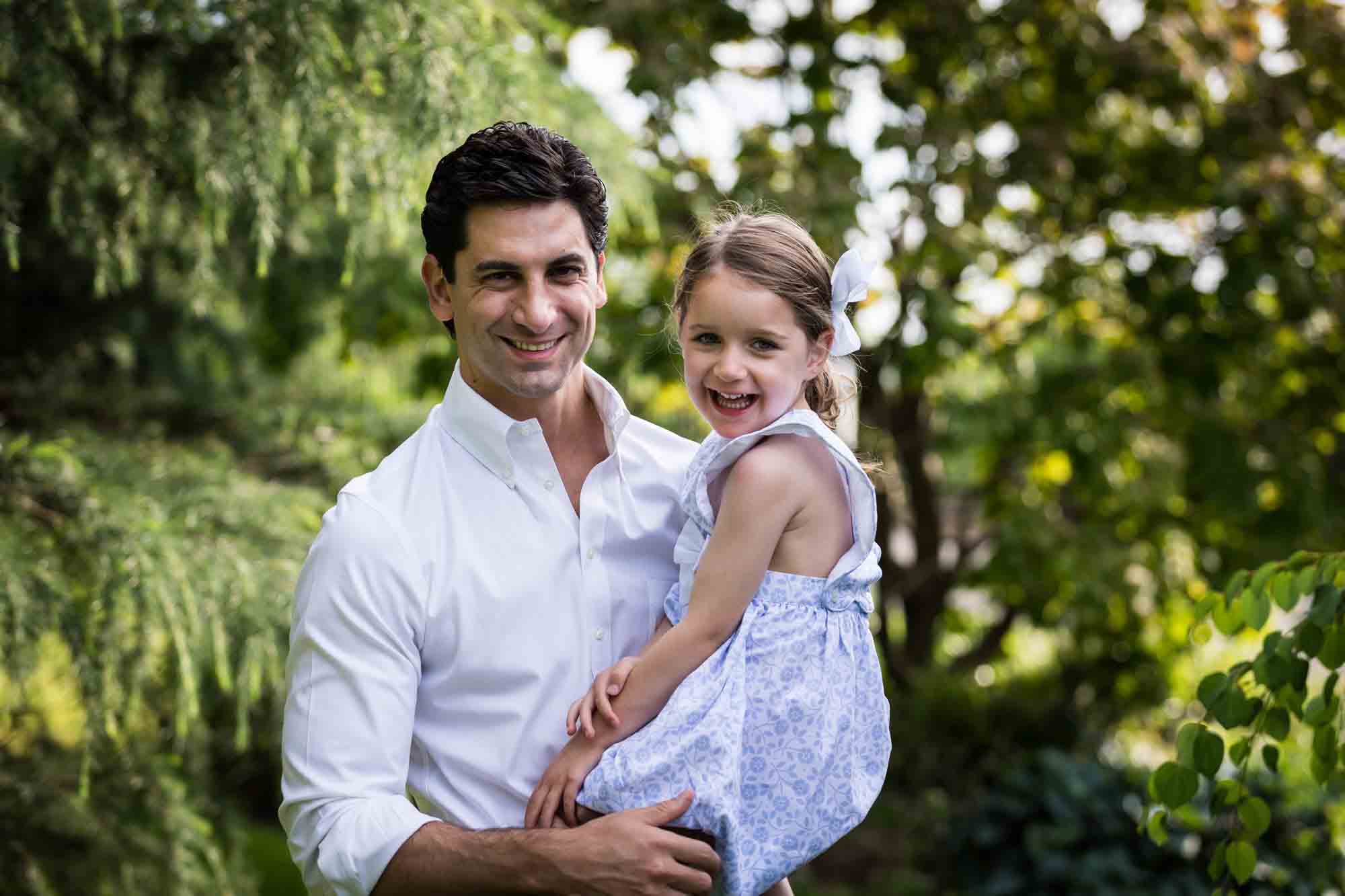 Man wearing white shirt holding little girl in front of trees during a Narrows Botanical Gardens family portrait session