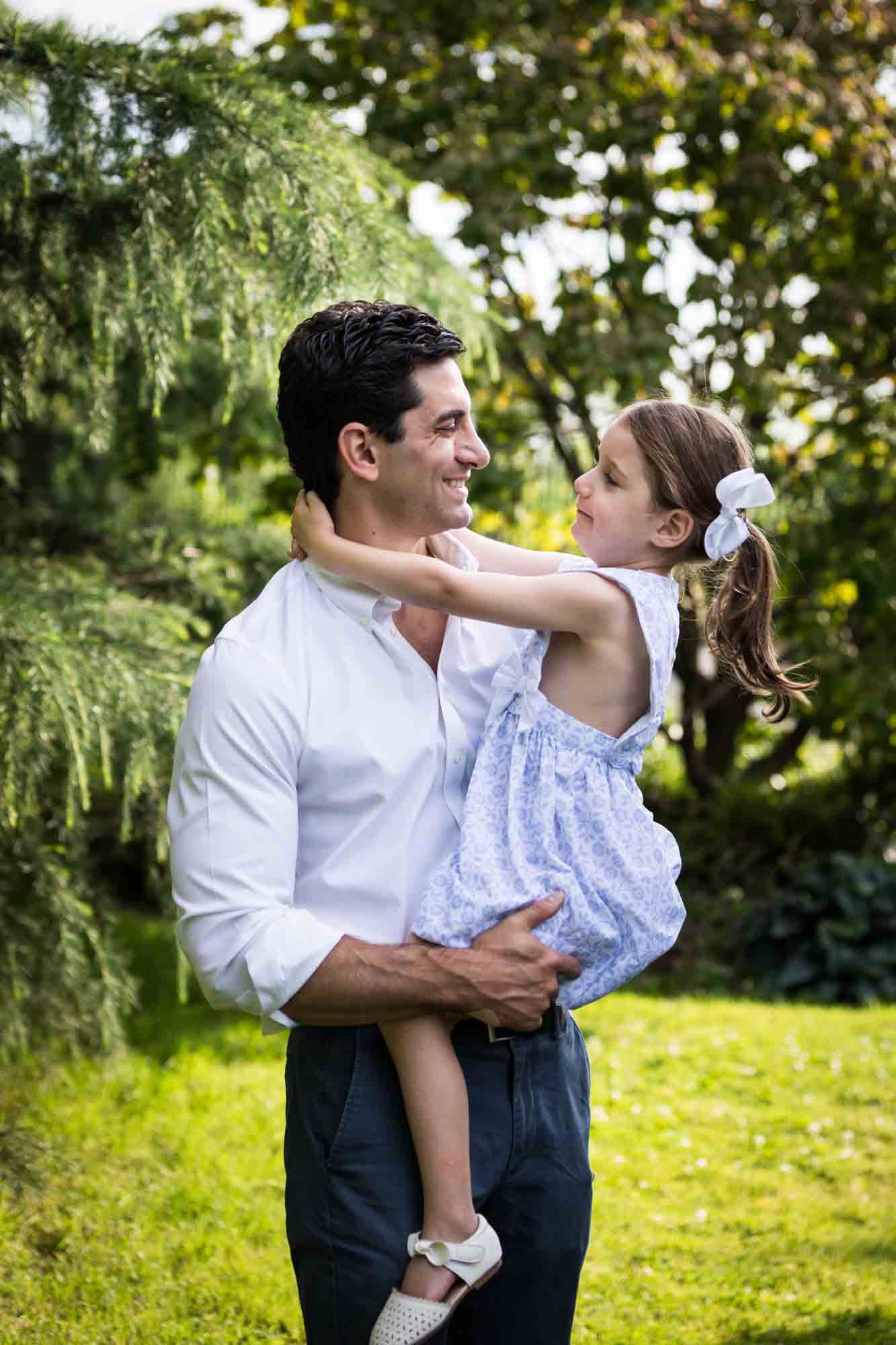 Man wearing white shirt holding little girl in front of trees during a Narrows Botanical Gardens family portrait session