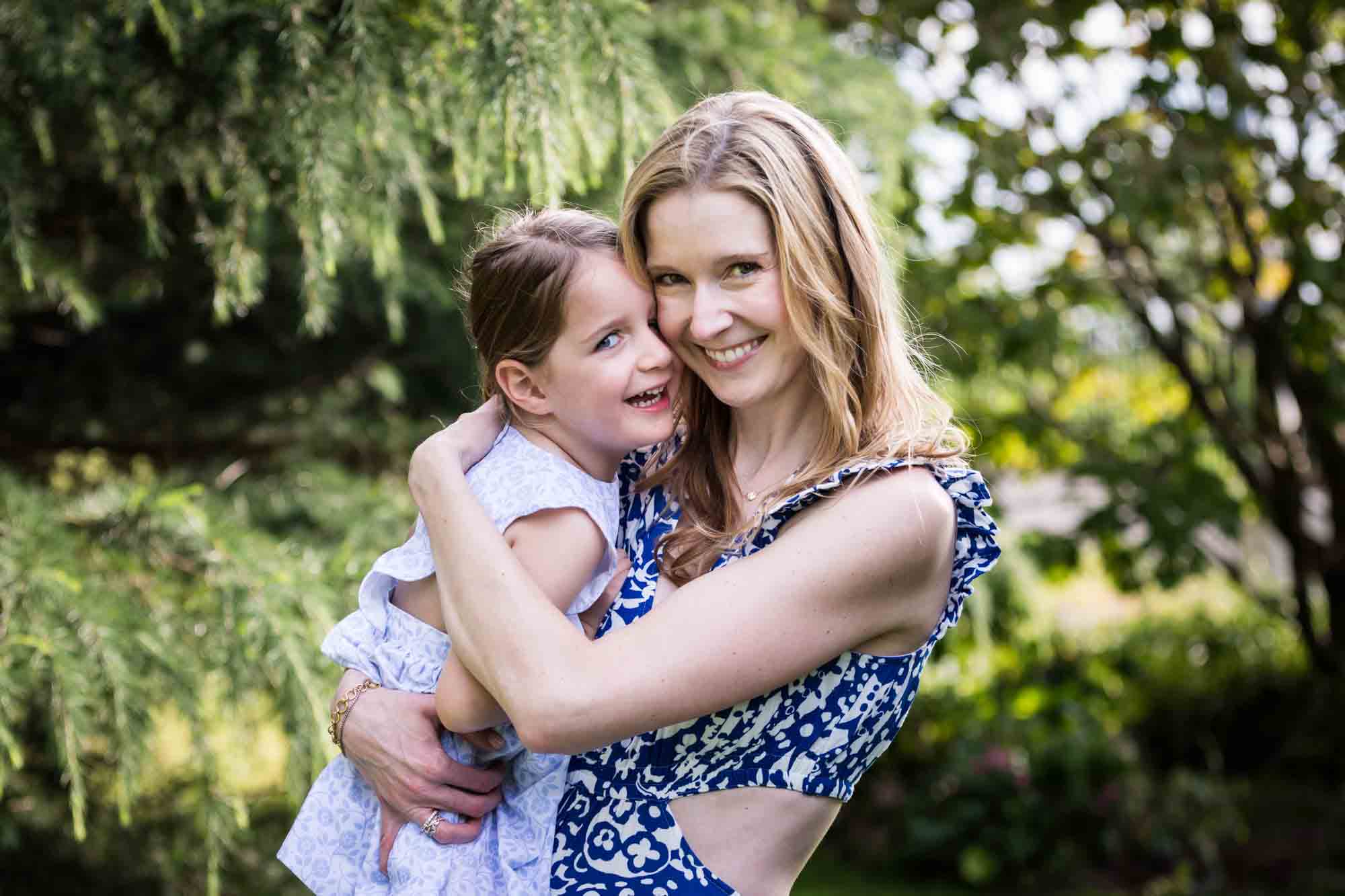 Blonde mother in blue dress holding little girl in front of trees during a Narrows Botanical Gardens family portrait session