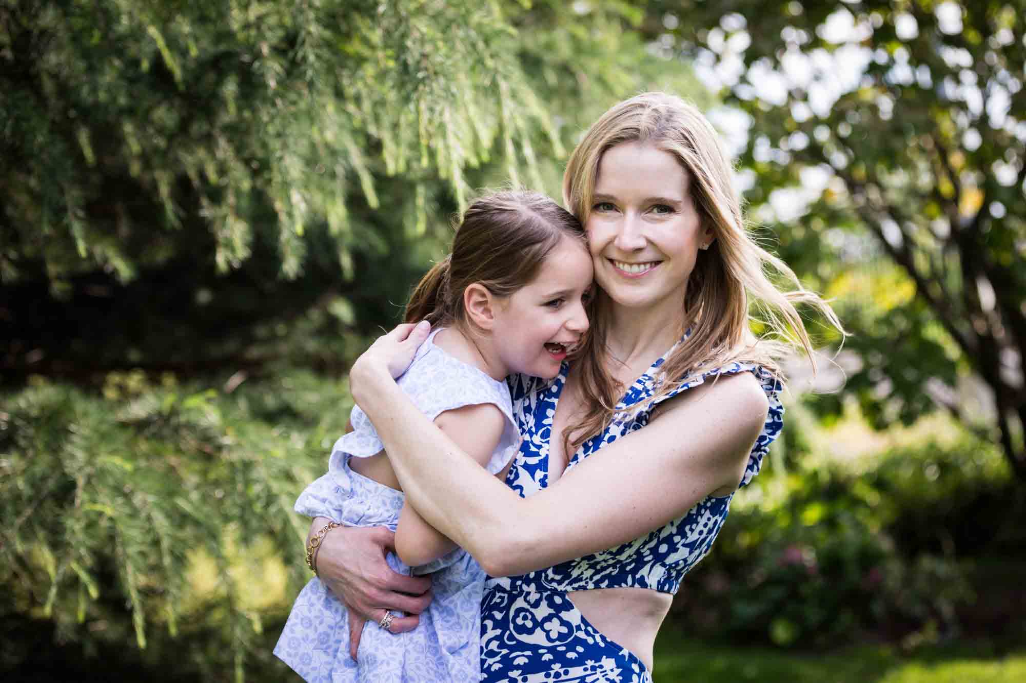 Blonde mother in blue dress holding little girl in front of trees during a Narrows Botanical Gardens family portrait session