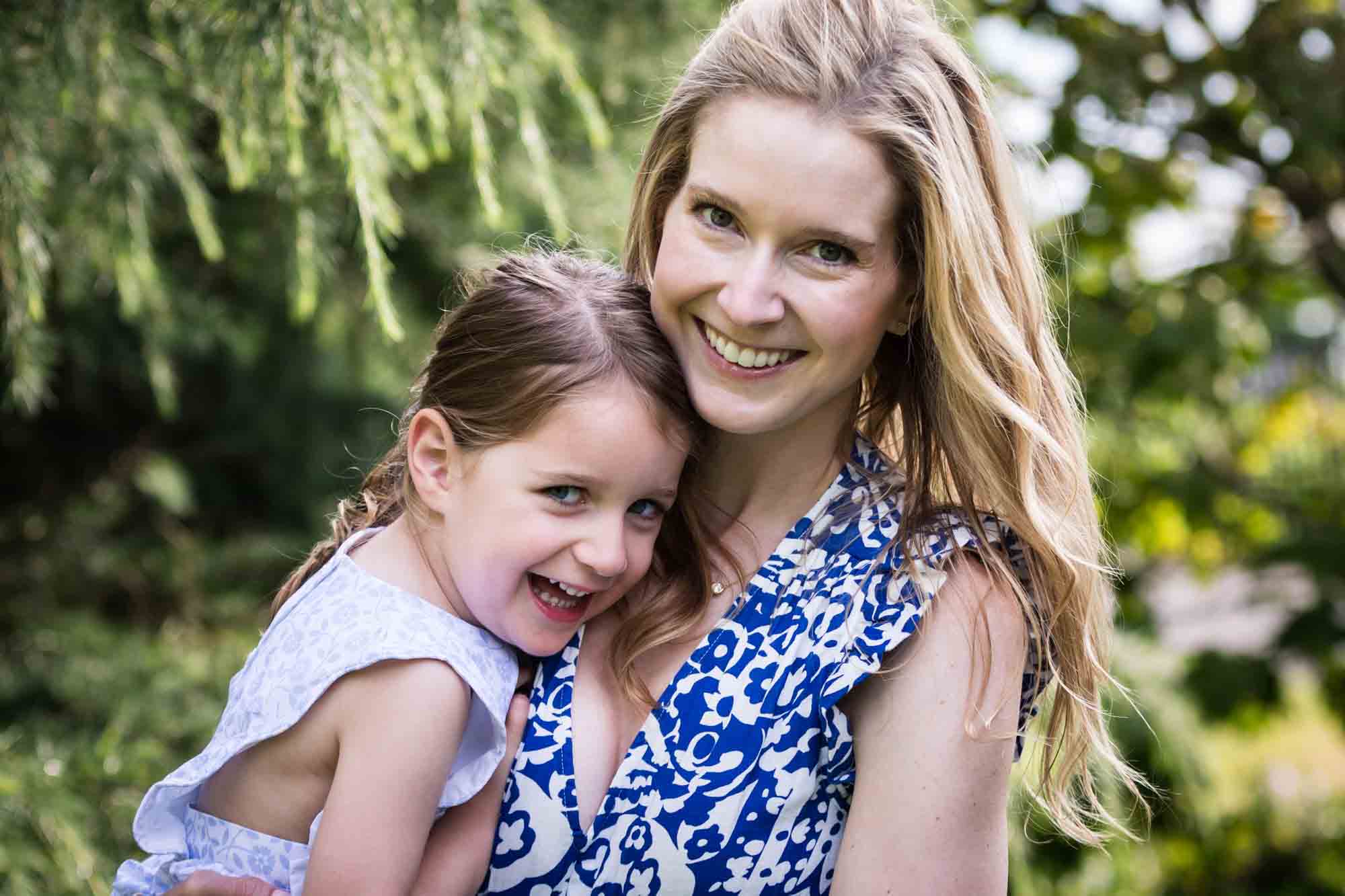 Blonde mother in blue dress holding little girl in front of trees during a Narrows Botanical Gardens family portrait session
