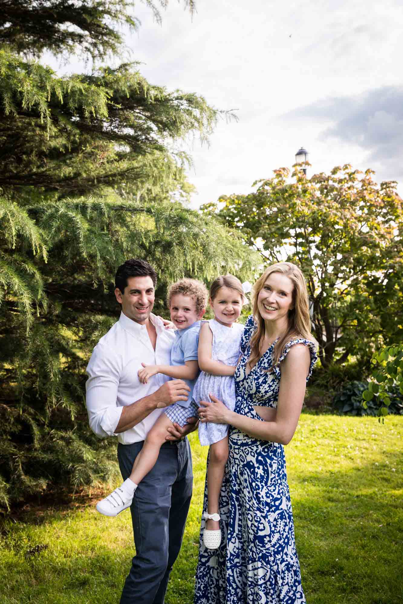 Parents holding little boy and girl in front of trees during a Narrows Botanical Gardens family portrait session