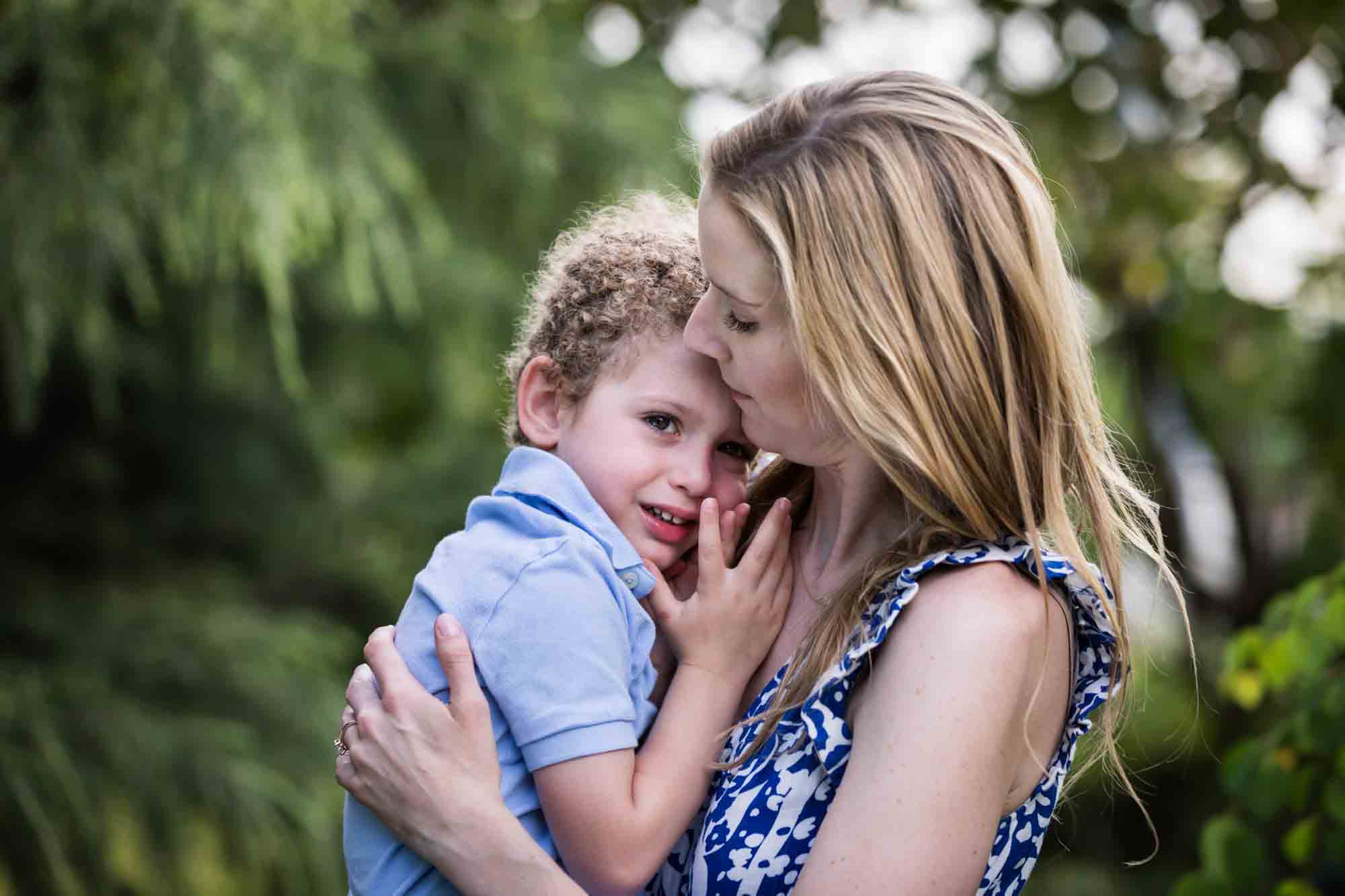 Blonde mother holding little boy with curly hair in front of a tree during a Narrows Botanical Gardens family portrait session