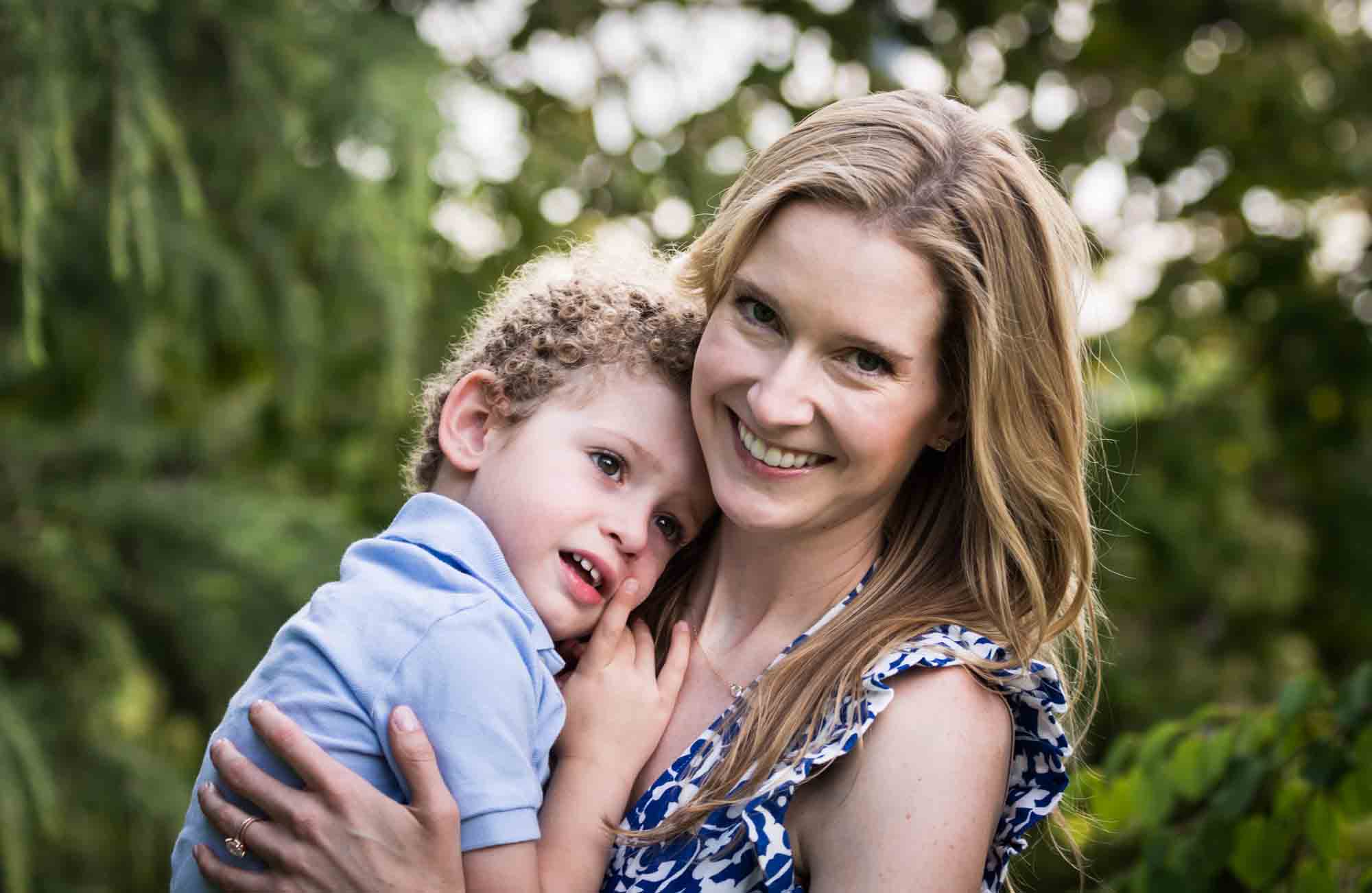 Blonde mother holding little boy with curly hair in front of a tree during a Narrows Botanical Gardens family portrait session