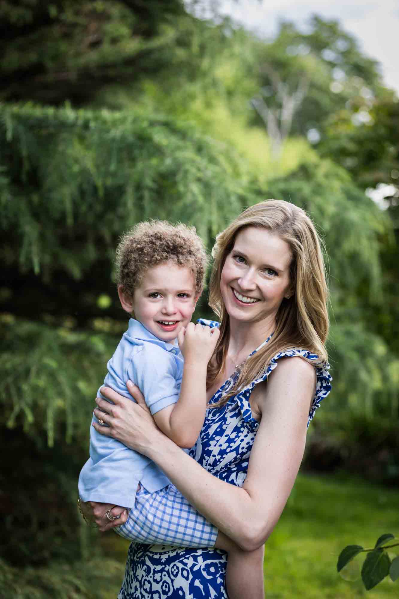 Blonde mother holding little boy with curly hair in front of a tree during a Narrows Botanical Gardens family portrait session