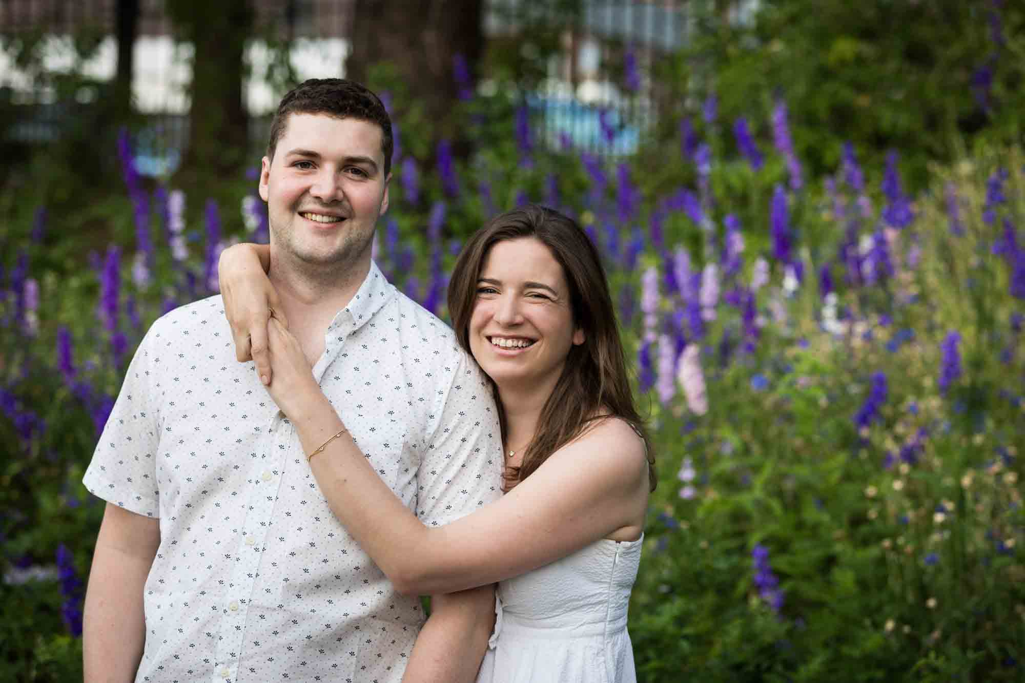 Woman hugging man with arms around his neck in front of purple flowers during a Narrows Botanical Gardens family portrait session
