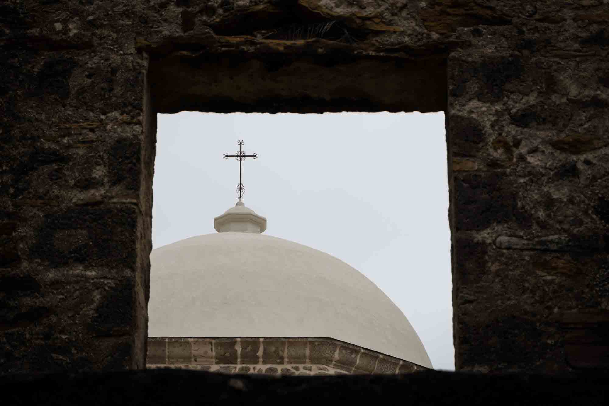 Cross on top of church at Mission San Jose seen through stone window in San Antonio