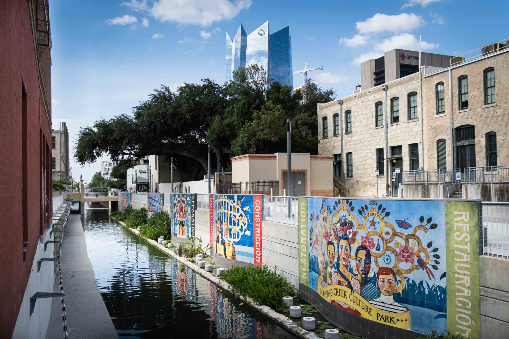 A canal in front of colorful murals in downtown San Antonio