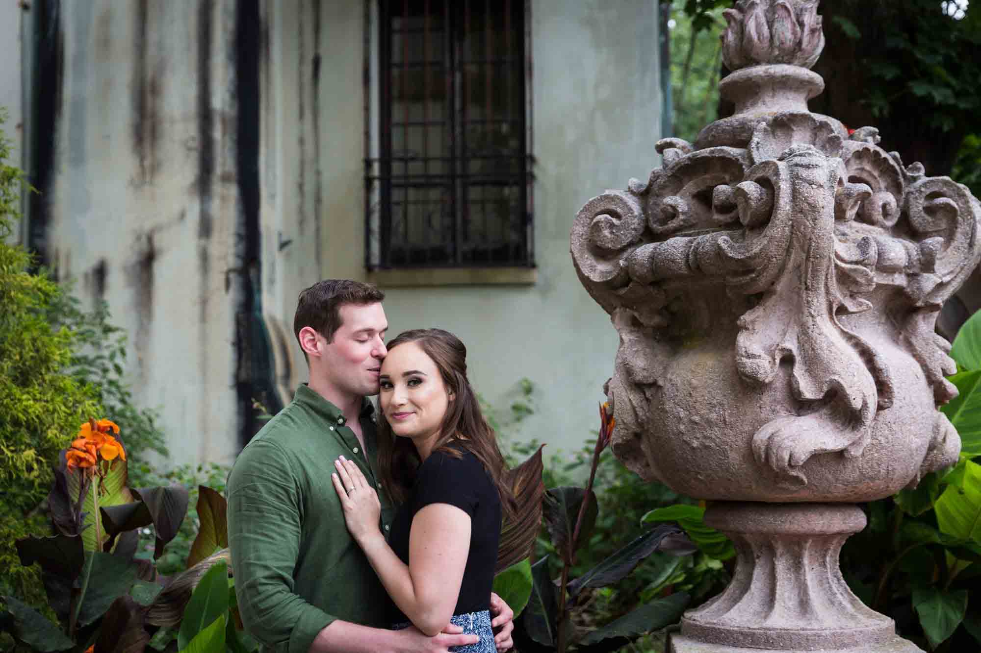Vanderbilt Museum engagement photos of man kissing woman on side of head with stone urn