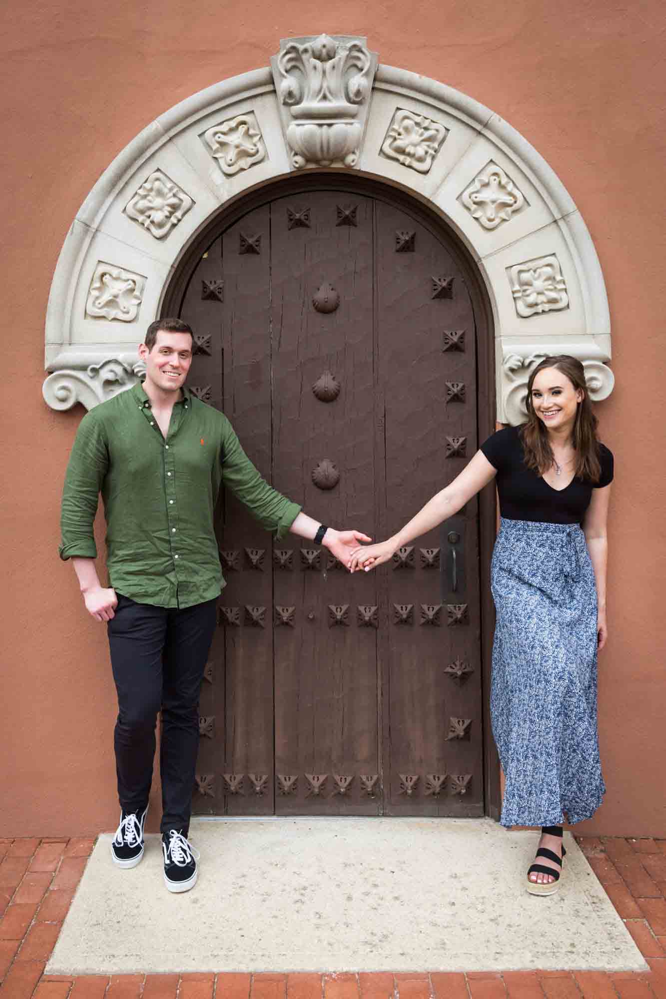 Couple holding hands in front of intricate wooden door at the Vanderbilt Museum