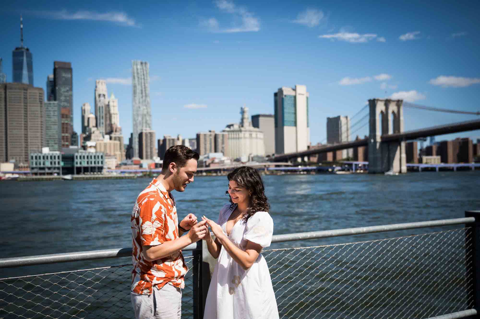 Couple looking at engagement ring in front of waterfront in Brooklyn Bridge Park