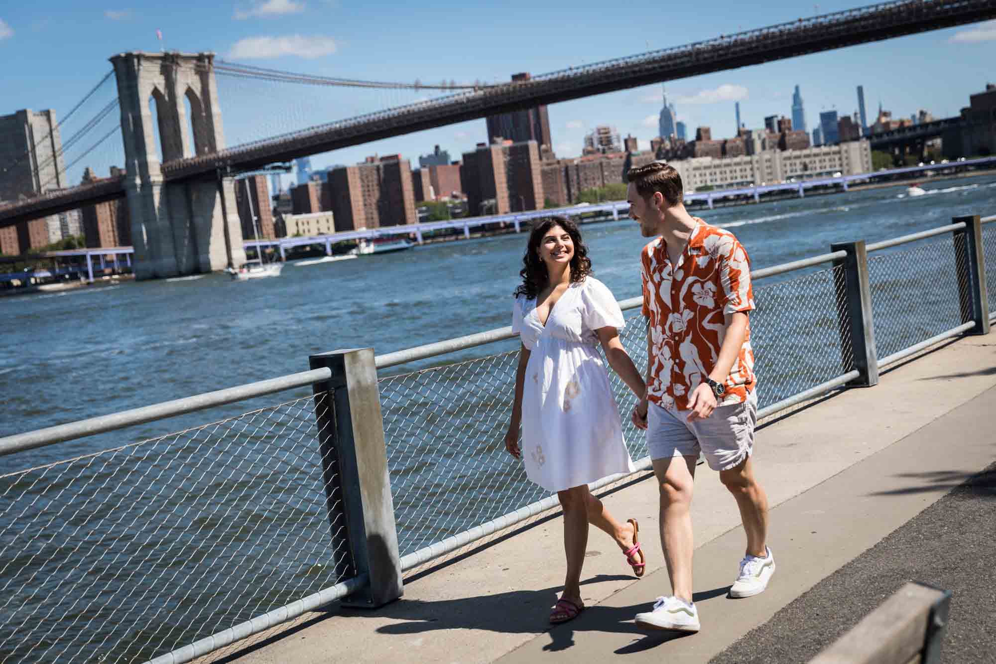 Couple walking hand-in-hand by waterfront in Brooklyn Bridge Park
