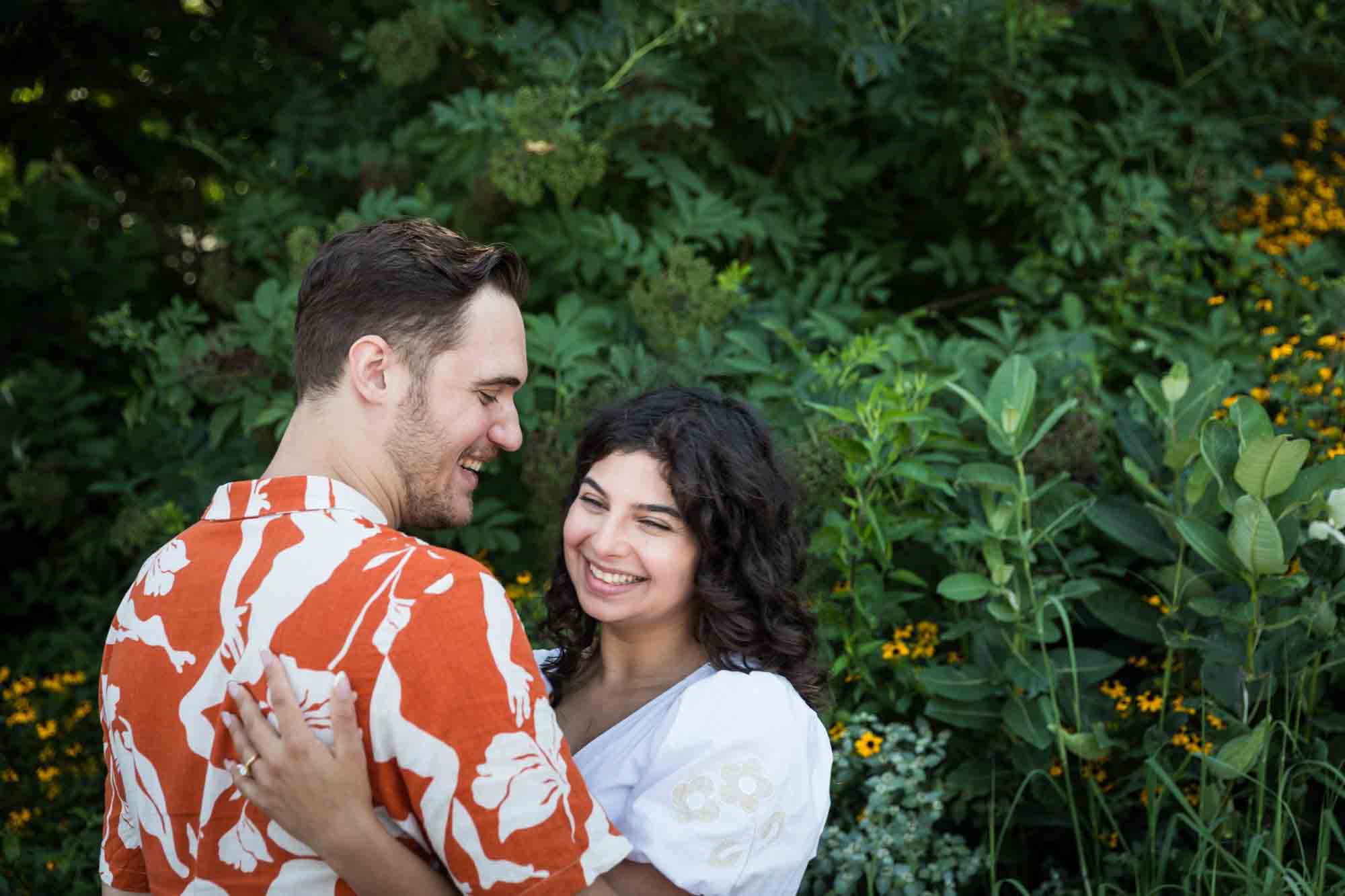 Couple laughing in front of green bushes in Brooklyn Bridge Park