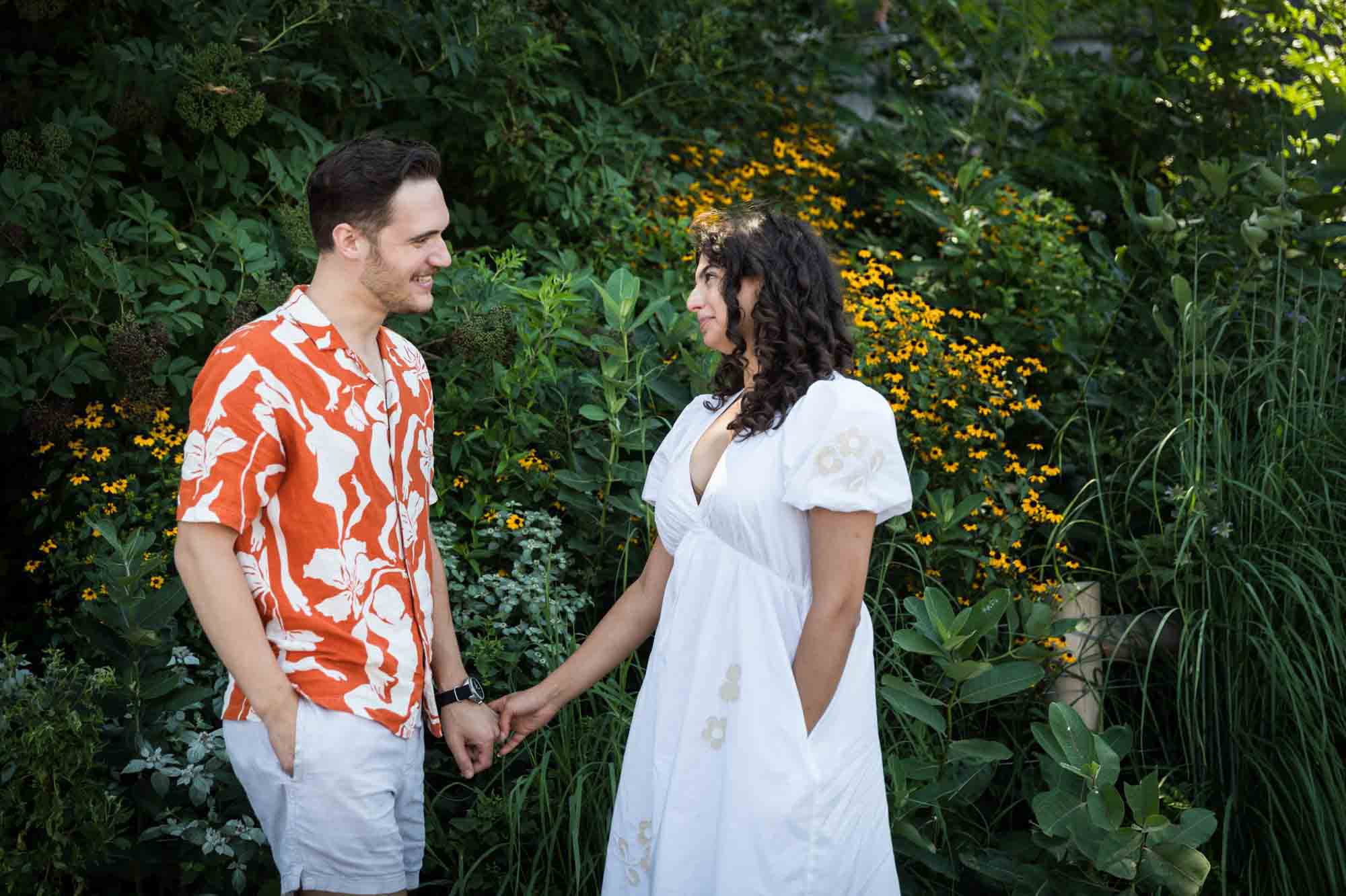 Couple holding hands in front of green bushes in Brooklyn Bridge Park