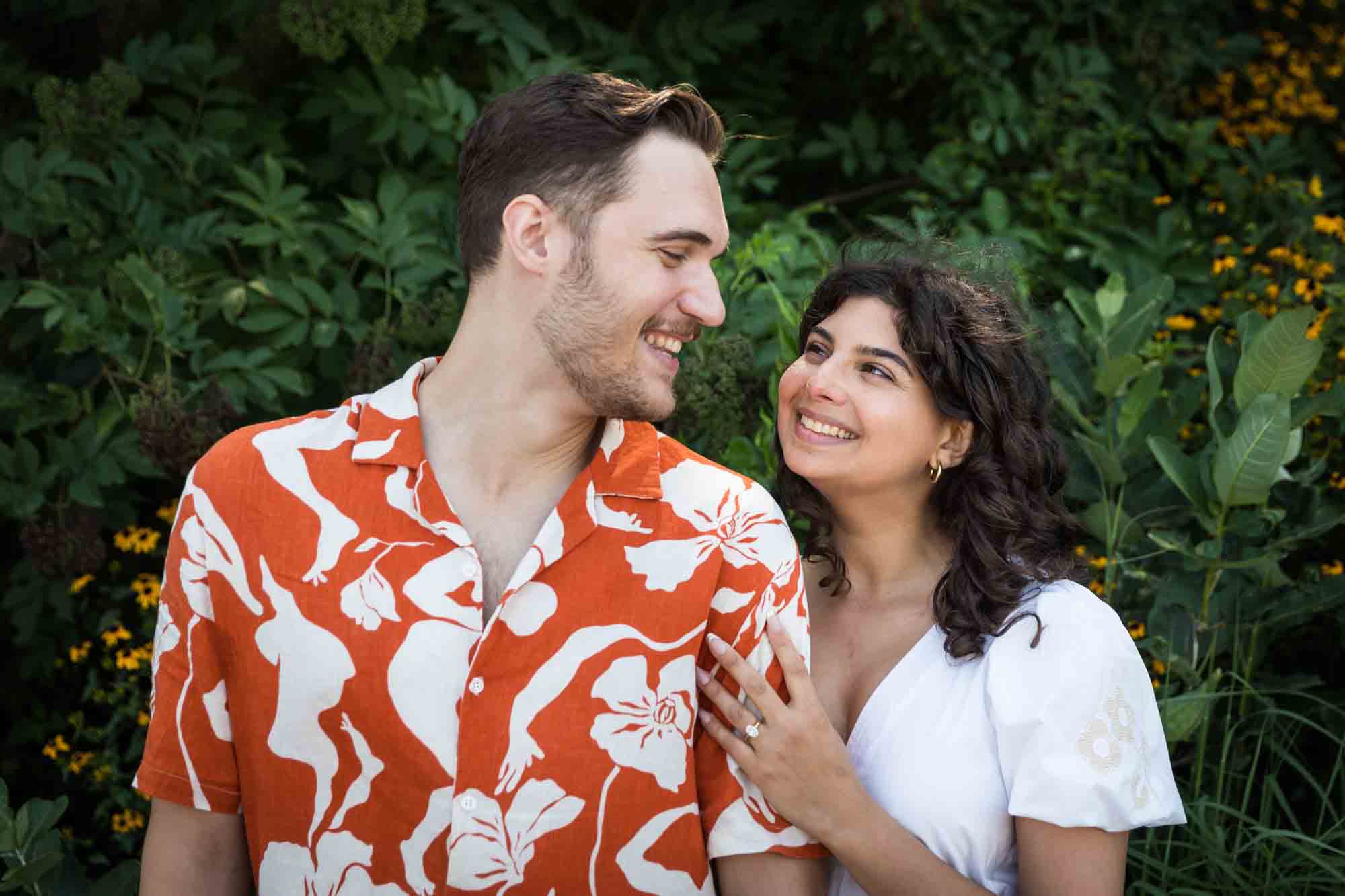 Couple laughing in front of green bushes in Brooklyn Bridge Park