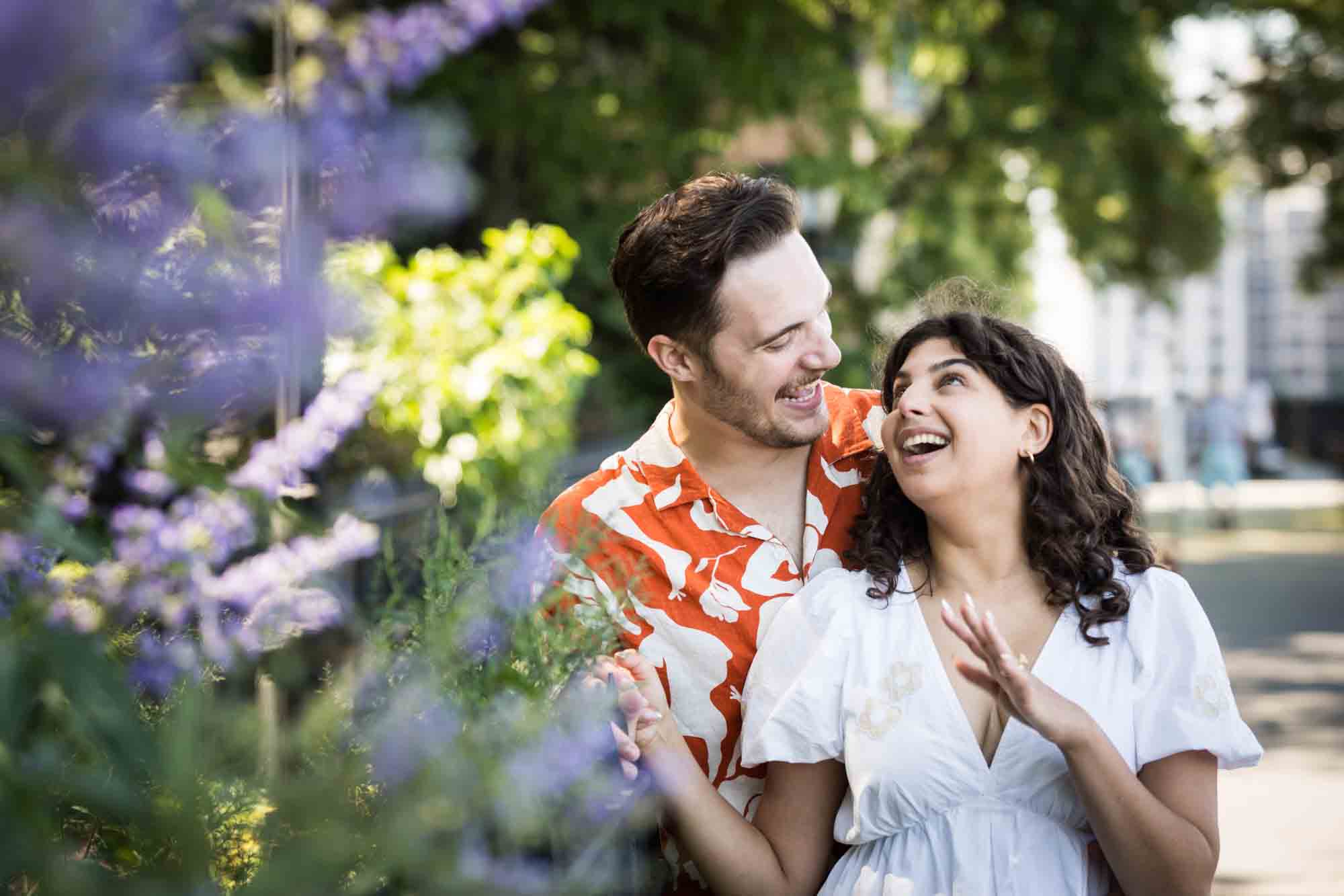 Couple laughing behind purple flowers during a Brooklyn Heights surprise proposal