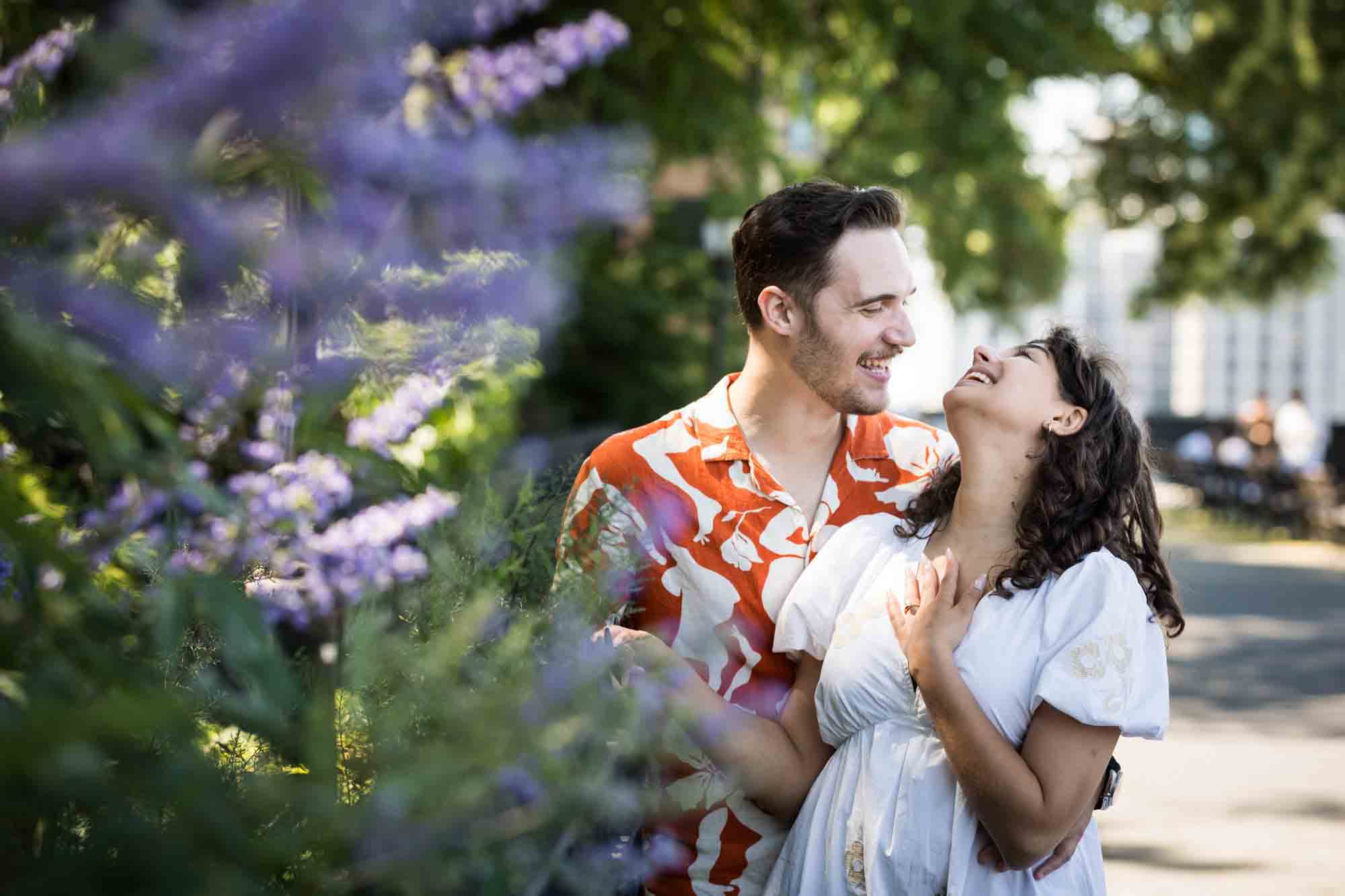 Couple laughing behind purple flowers during a Brooklyn Heights surprise proposal