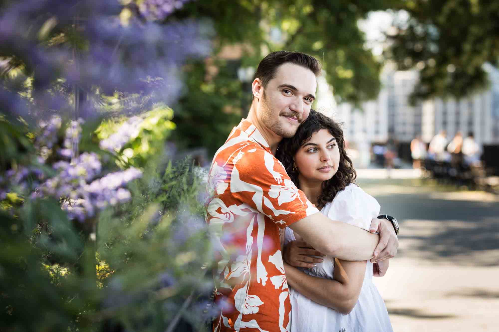 Couple hugging behind purple flowers during a Brooklyn Heights surprise proposal