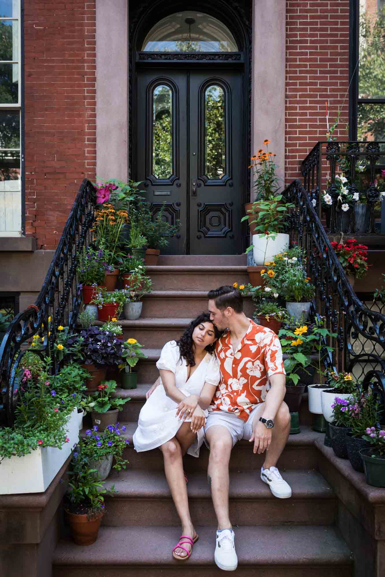 Couple hugging on brownstone staircase surrounded by flowers during a Brooklyn Heights surprise proposal