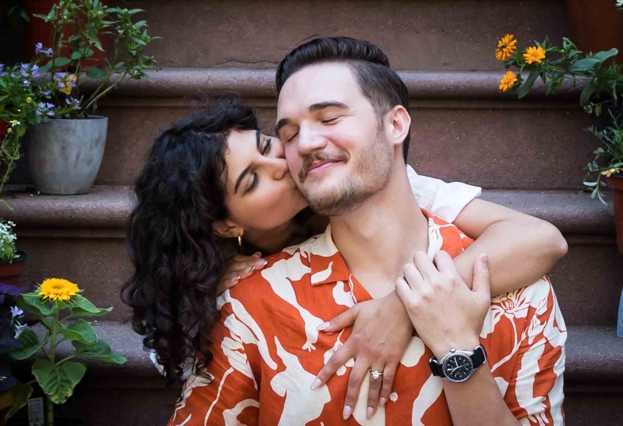 Woman kissing man on cheek on brownstone staircase during a Brooklyn Heights surprise proposal