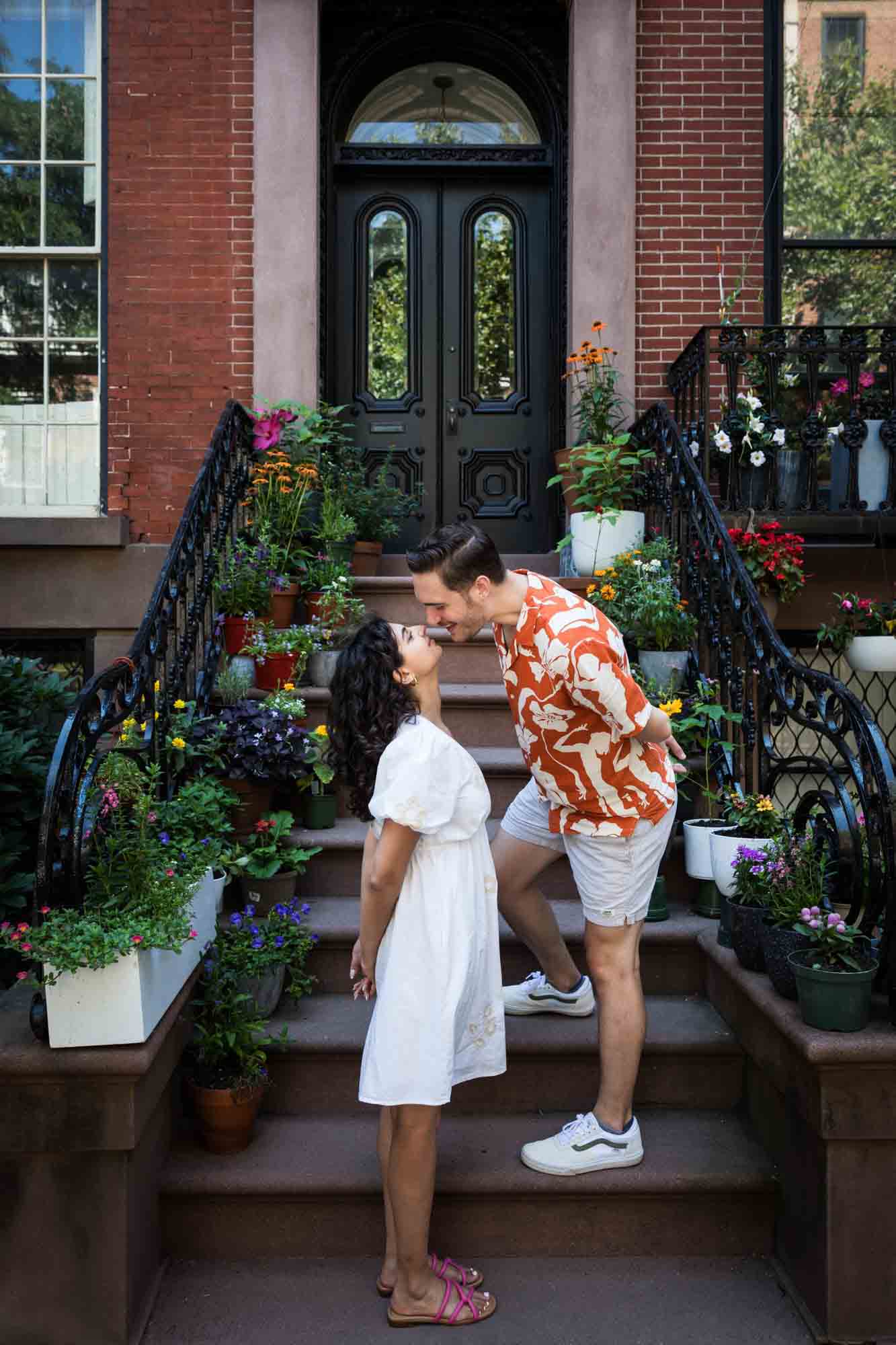 Couple kissing on brownstone staircase surrounded by flowers during a Brooklyn Heights surprise proposal