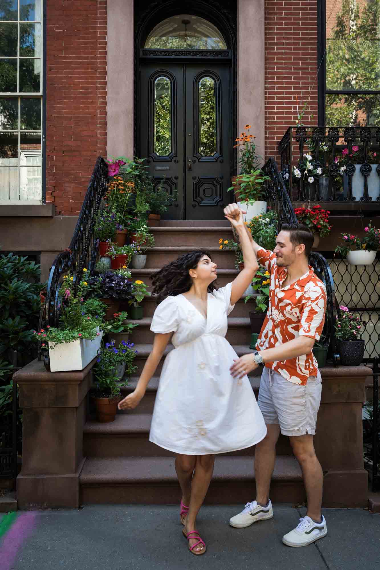 Couple dancing on brownstone staircase surrounded by flowers during a Brooklyn Heights surprise proposal