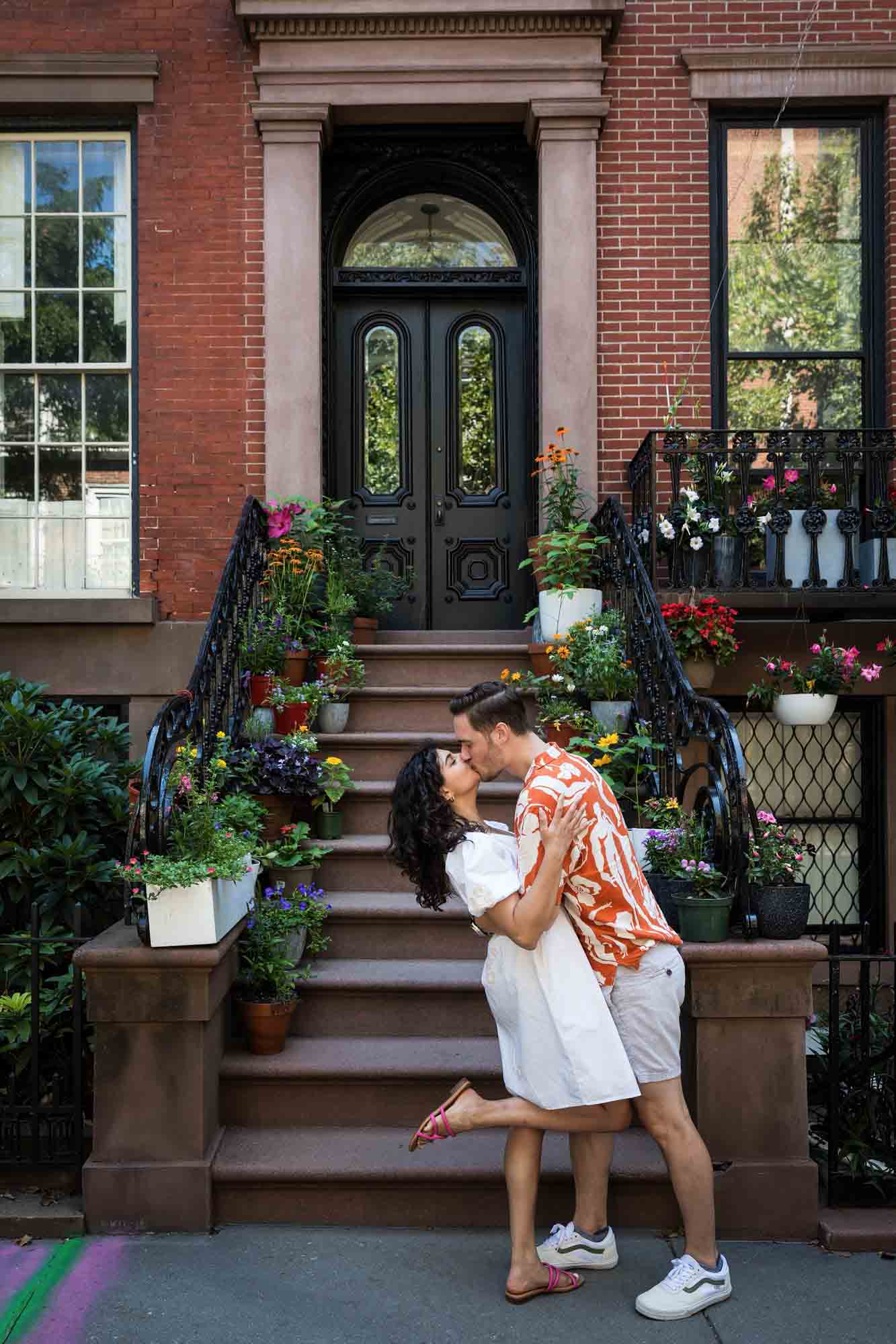 Couple hugging on brownstone staircase surrounded by flowers kissing a Brooklyn Heights surprise proposal