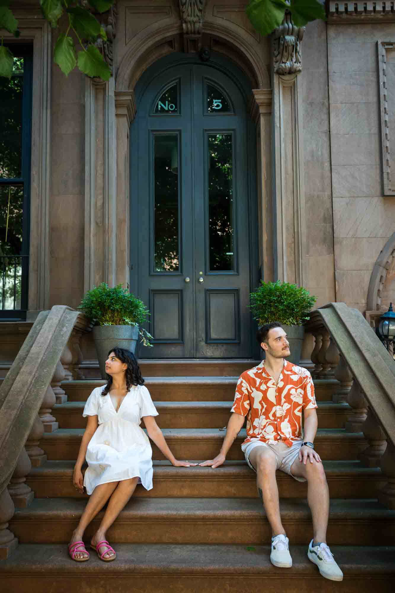 Couple sitting on brownstone staircase touching hands during a Brooklyn Heights surprise proposal