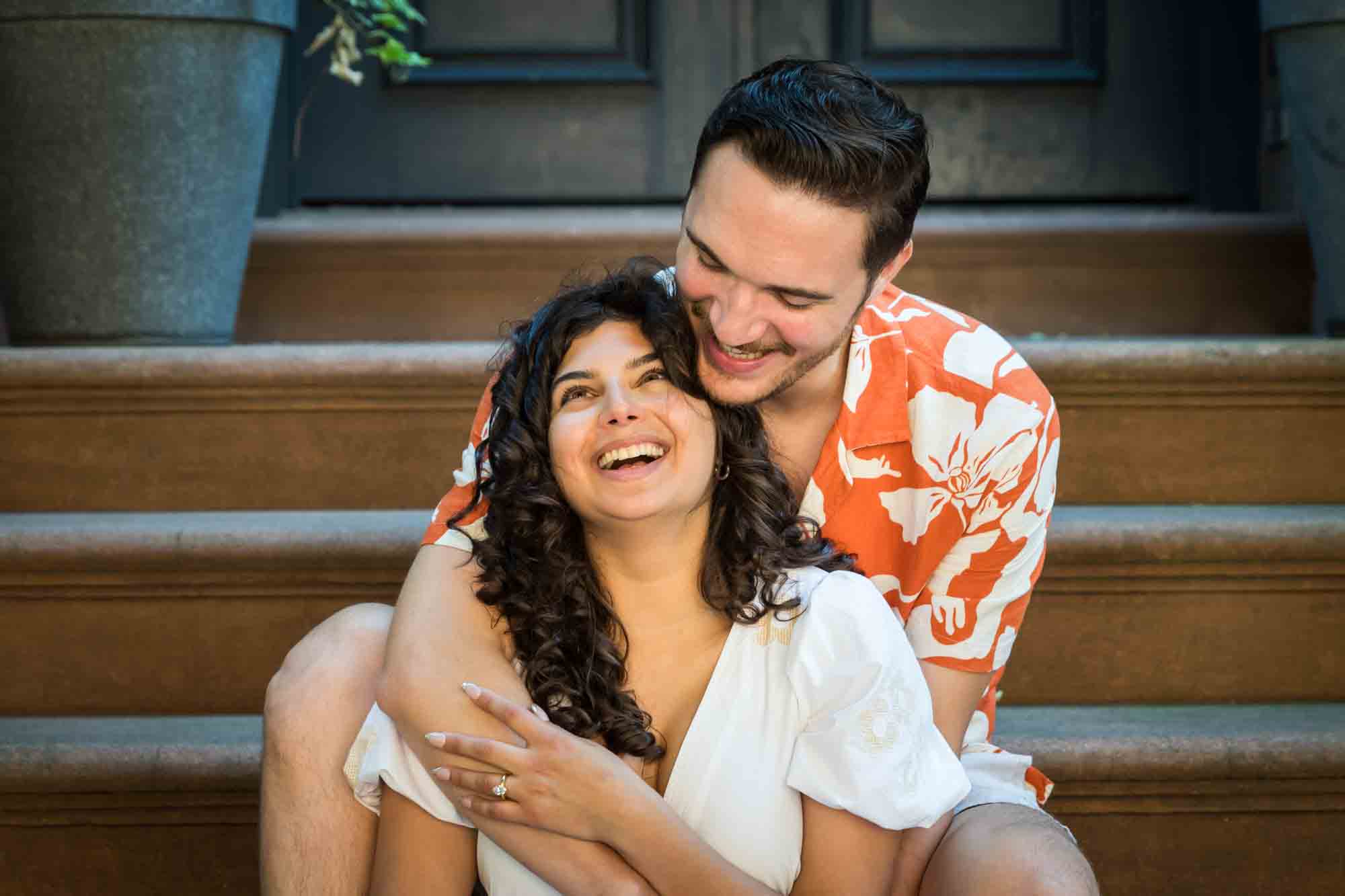 Couple laughing on brownstone staircase during a Brooklyn Heights surprise proposal
