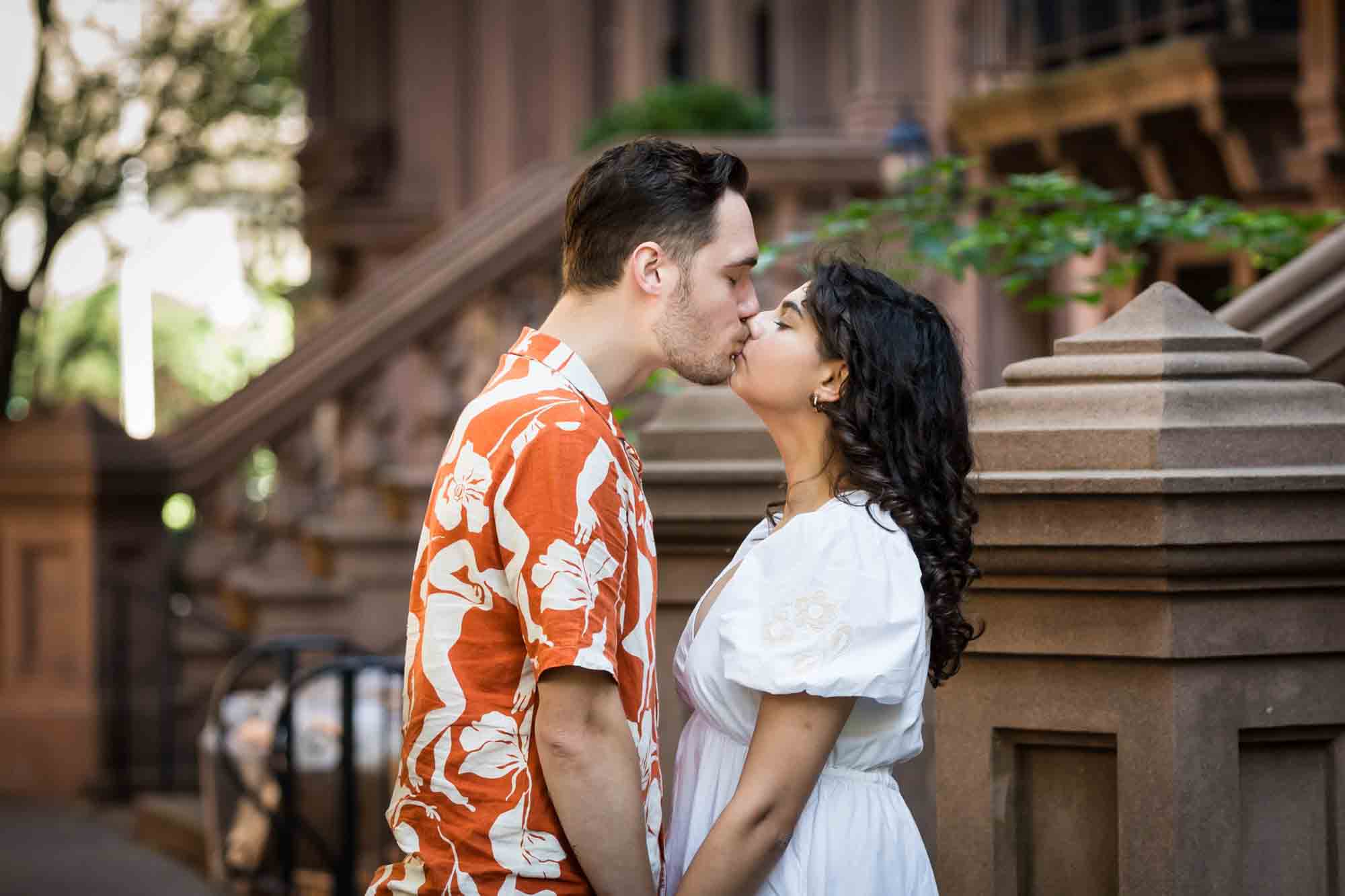 Couple kissing in front of brownstone staircase during a Brooklyn Heights surprise proposal